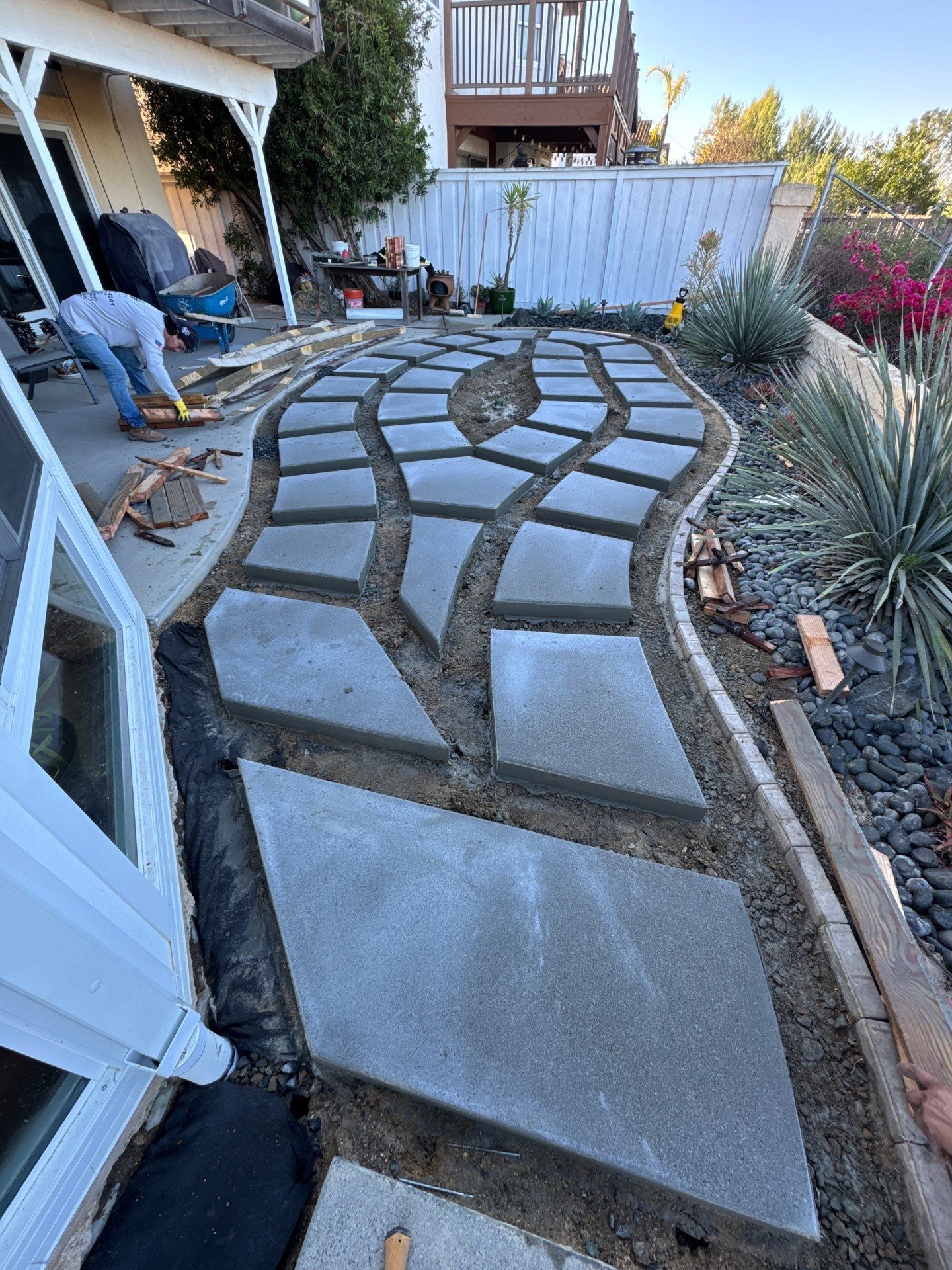 Pathway construction: Person laying stone pavers in a backyard with a curved path.