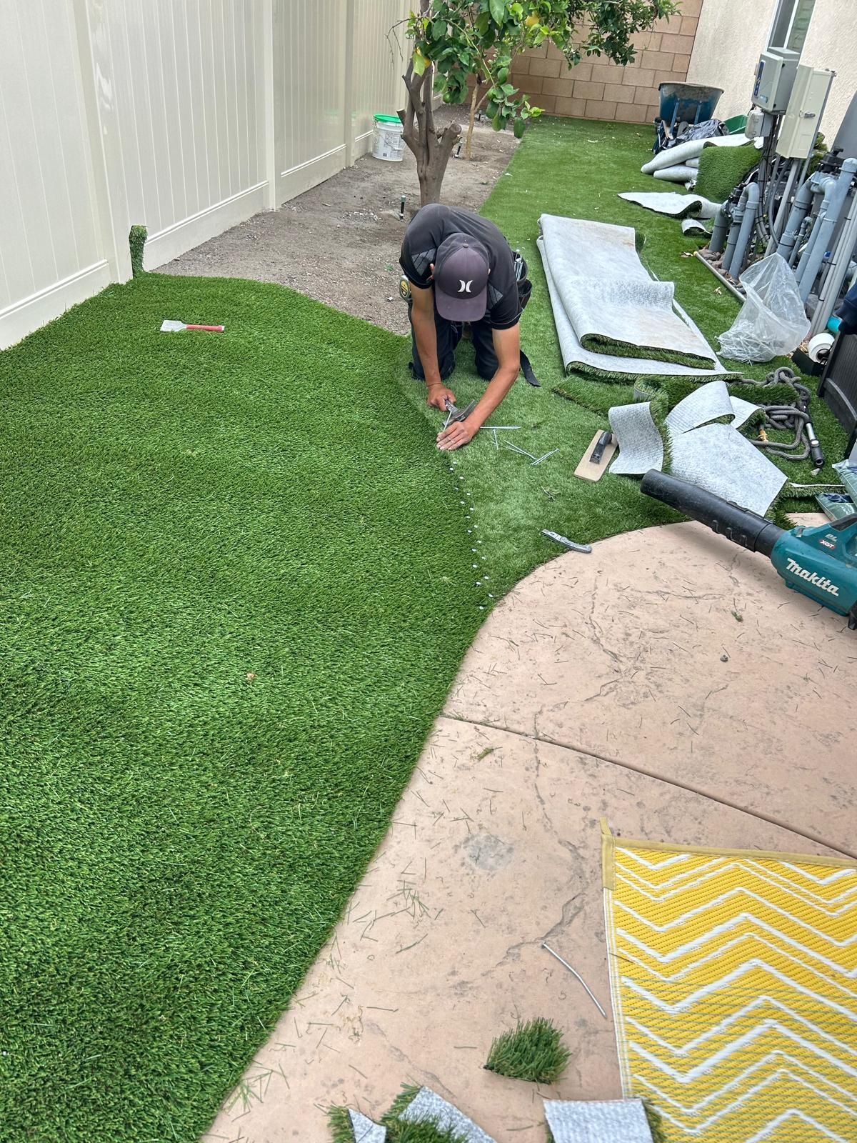 Person installing green artificial turf in a backyard, using a utility knife.
