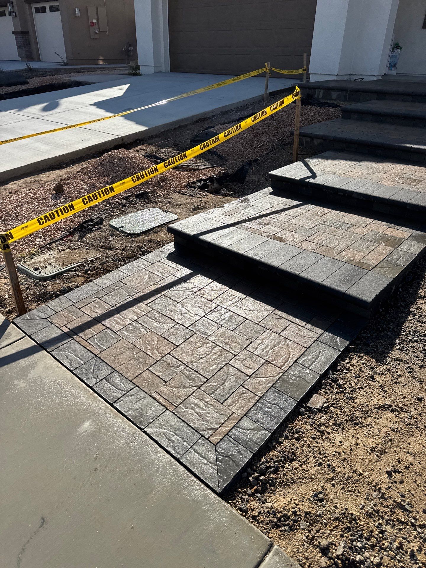 Concrete steps and walkway with patterned stone detail. Yellow caution tape surrounds the area, under construction.