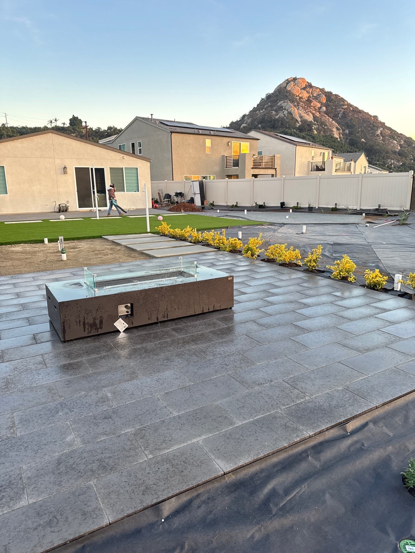 Patio with a fire pit, houses, and a mountain in the background. Someone walks through the yard.