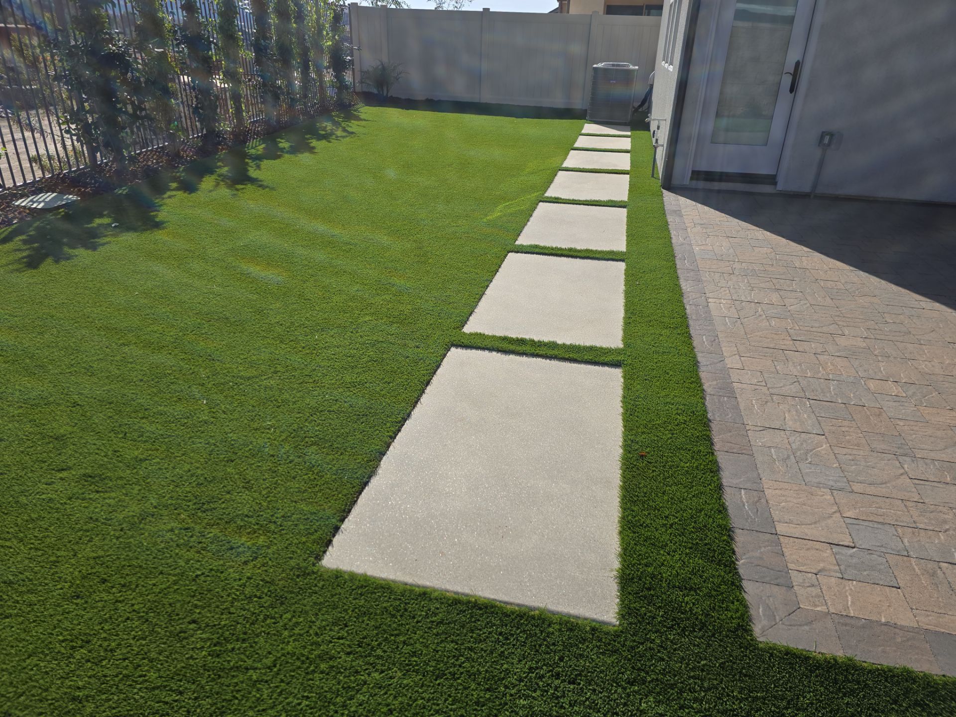 Green lawn with stepping stones leading to a trash can near a building's exterior.