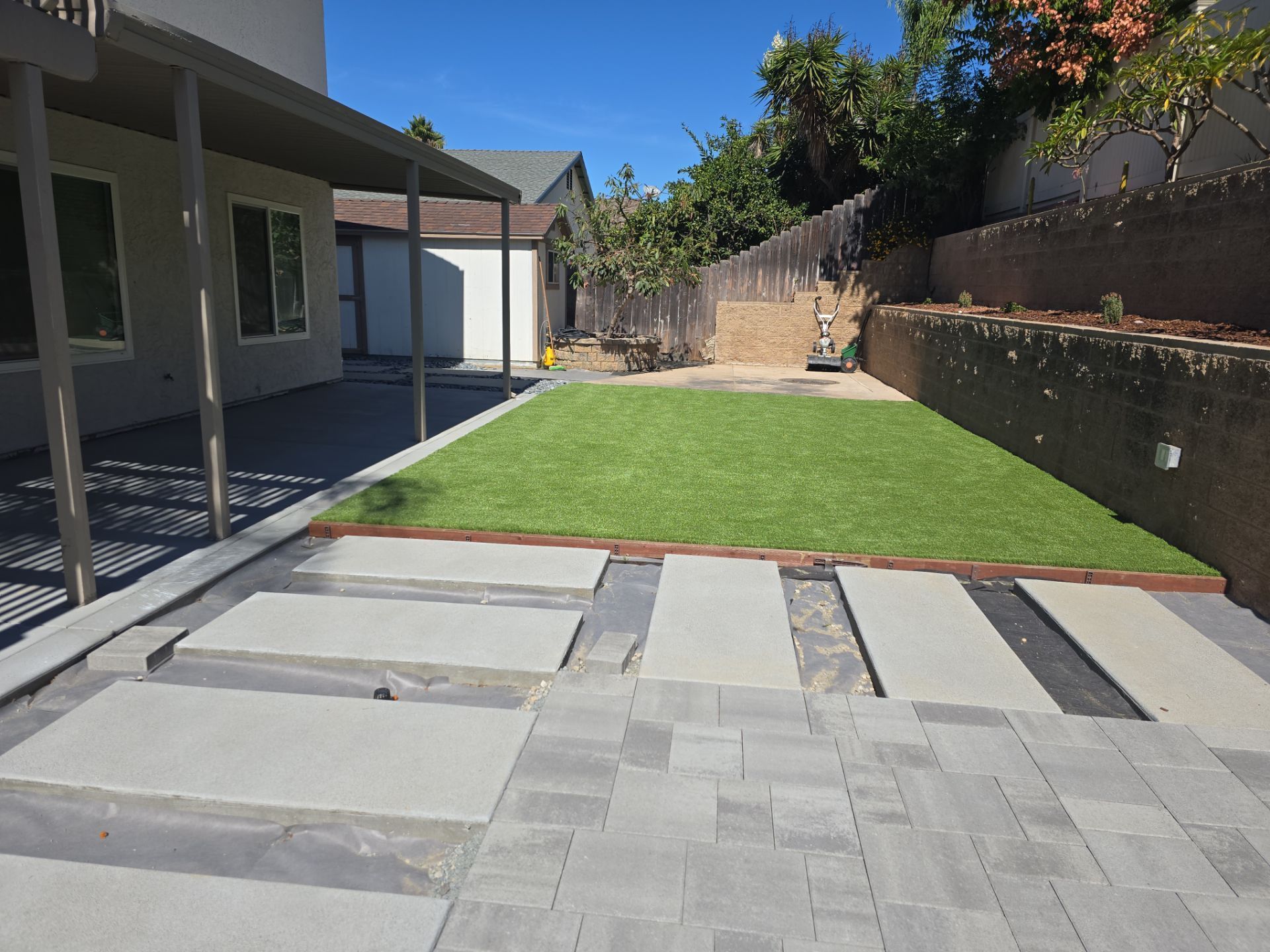 Backyard with a patio, steps, green turf, and a retaining wall.