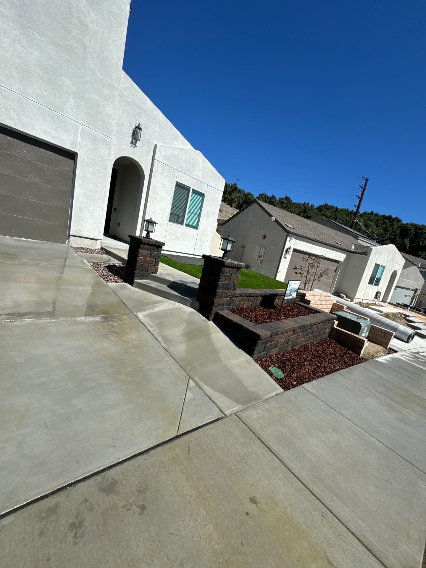 White stucco house with concrete driveway, landscaping, and a blue sky.