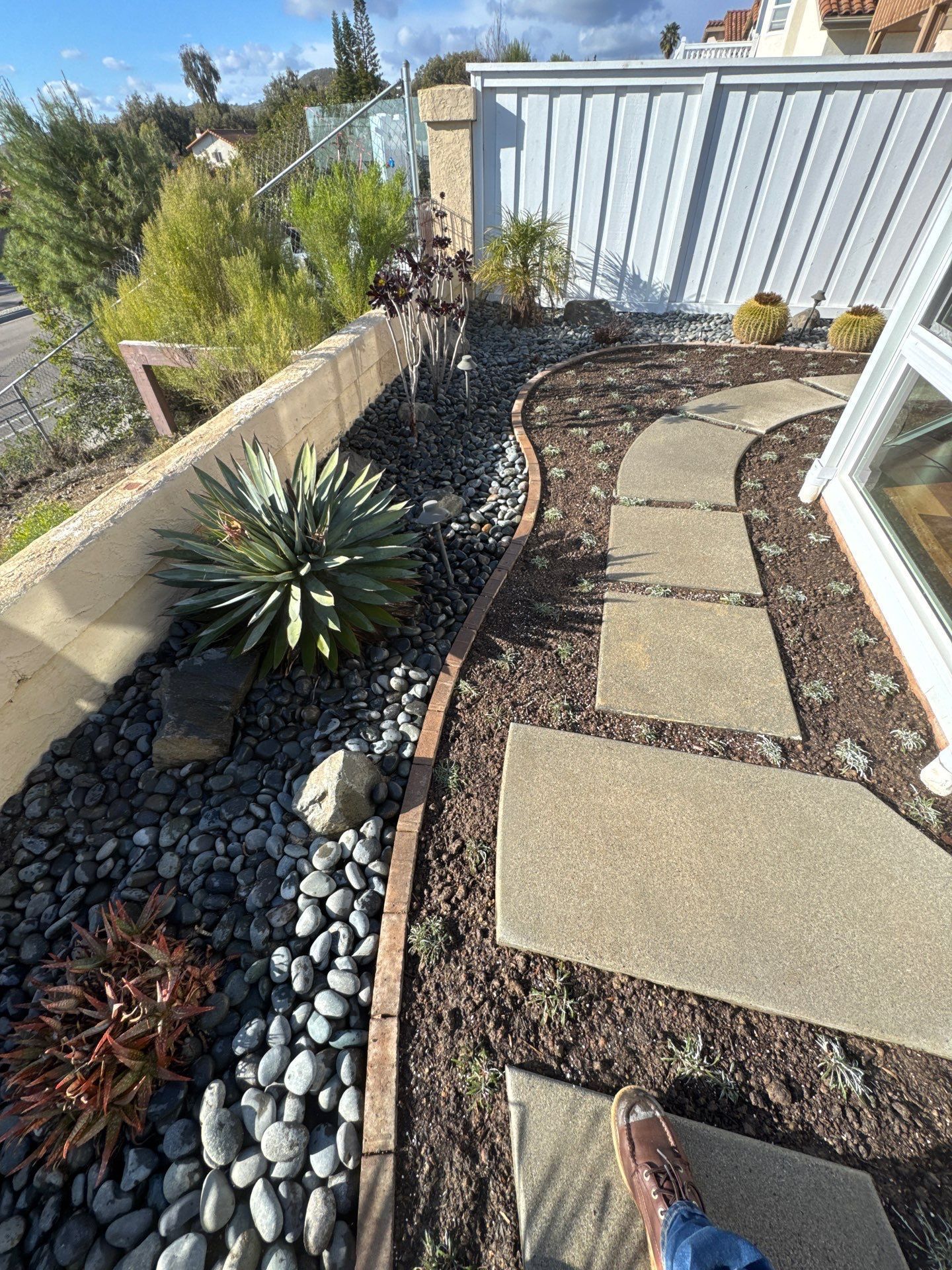 Landscaped garden path with stepping stones, bordered by plants, black stones, and wood edging.