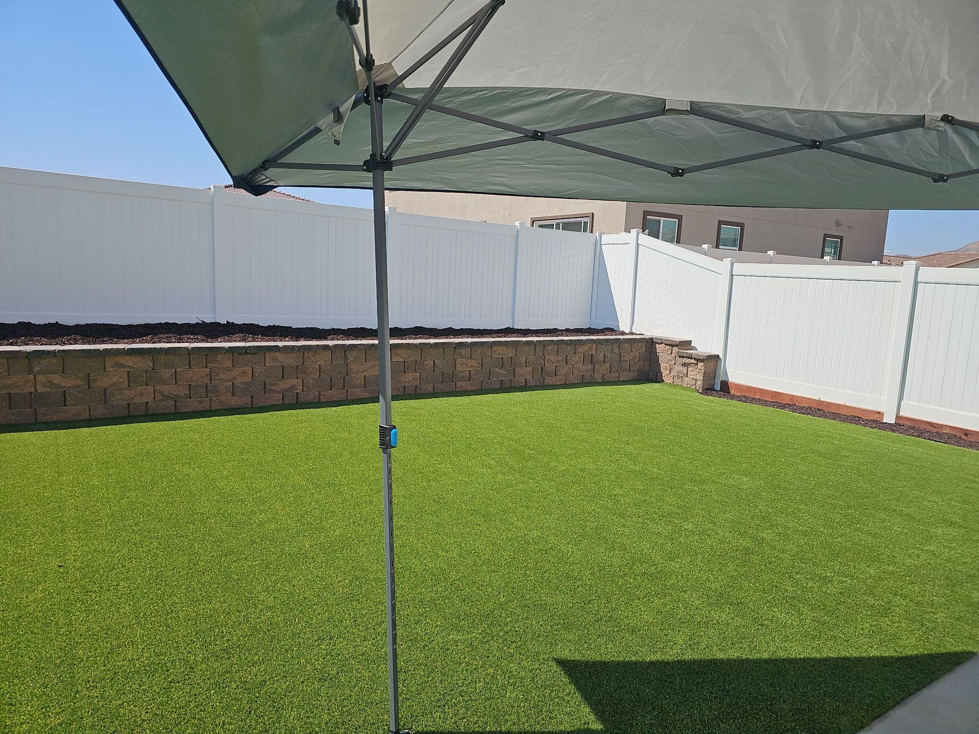 Green artificial turf backyard with white fence and retractable canopy.