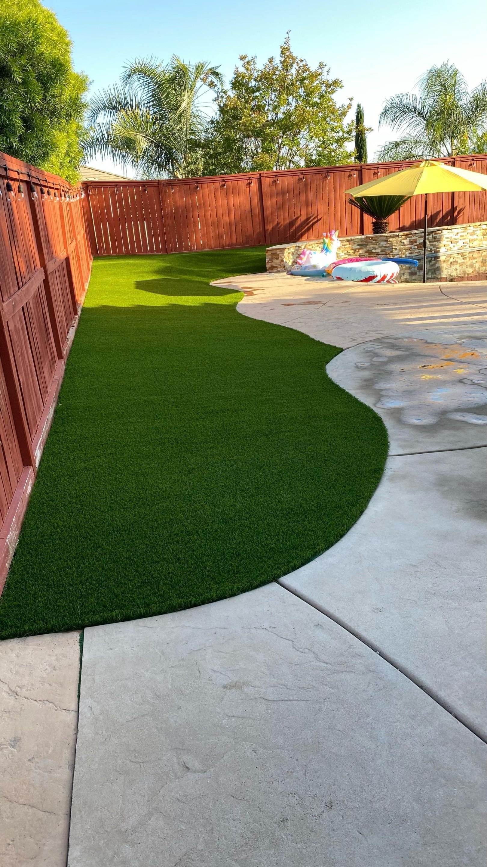 Green artificial turf in a backyard next to a brown fence and concrete patio.