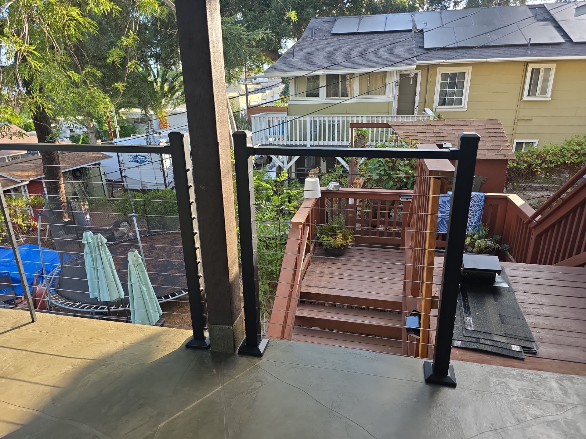 Deck with glass railing, stairs, and view of a house with solar panels and trees.