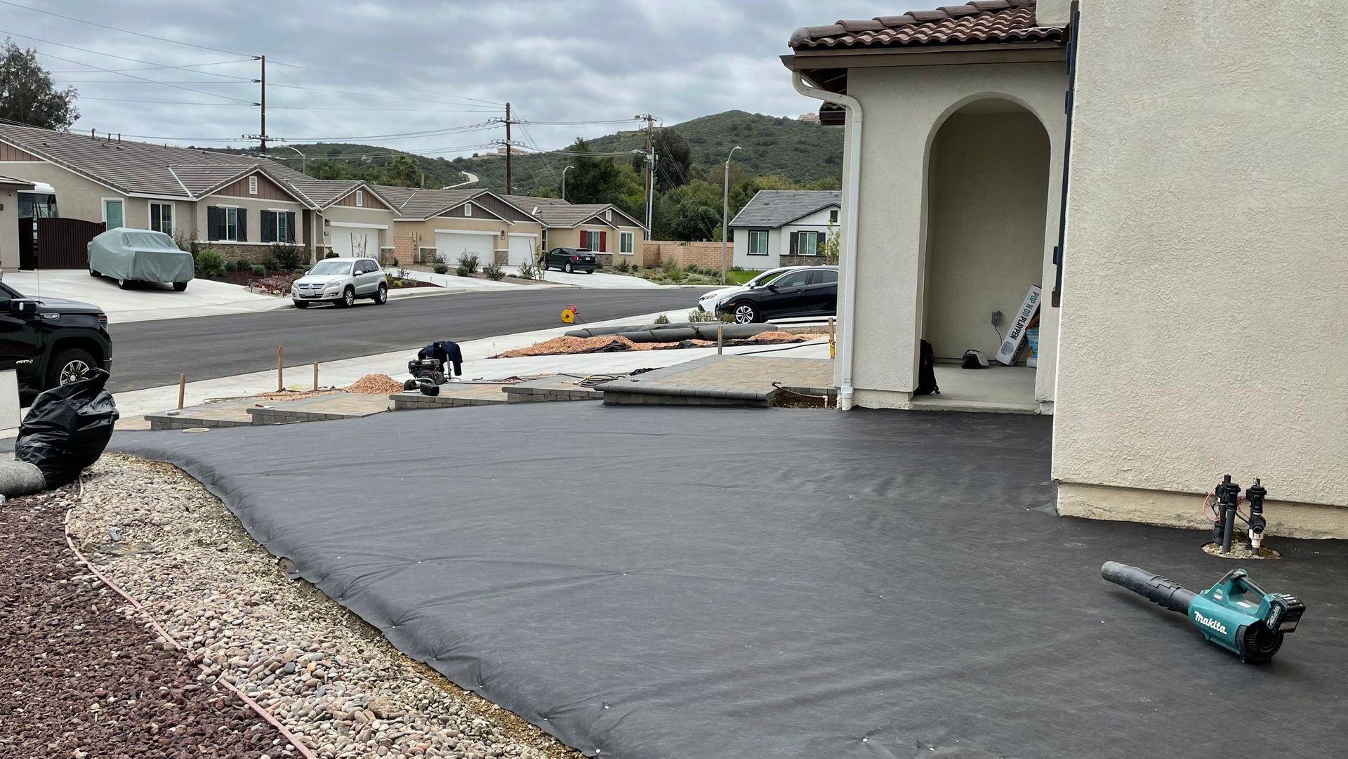 Driveway resurfacing in progress. Black asphalt, concrete, blower, residential street in background.