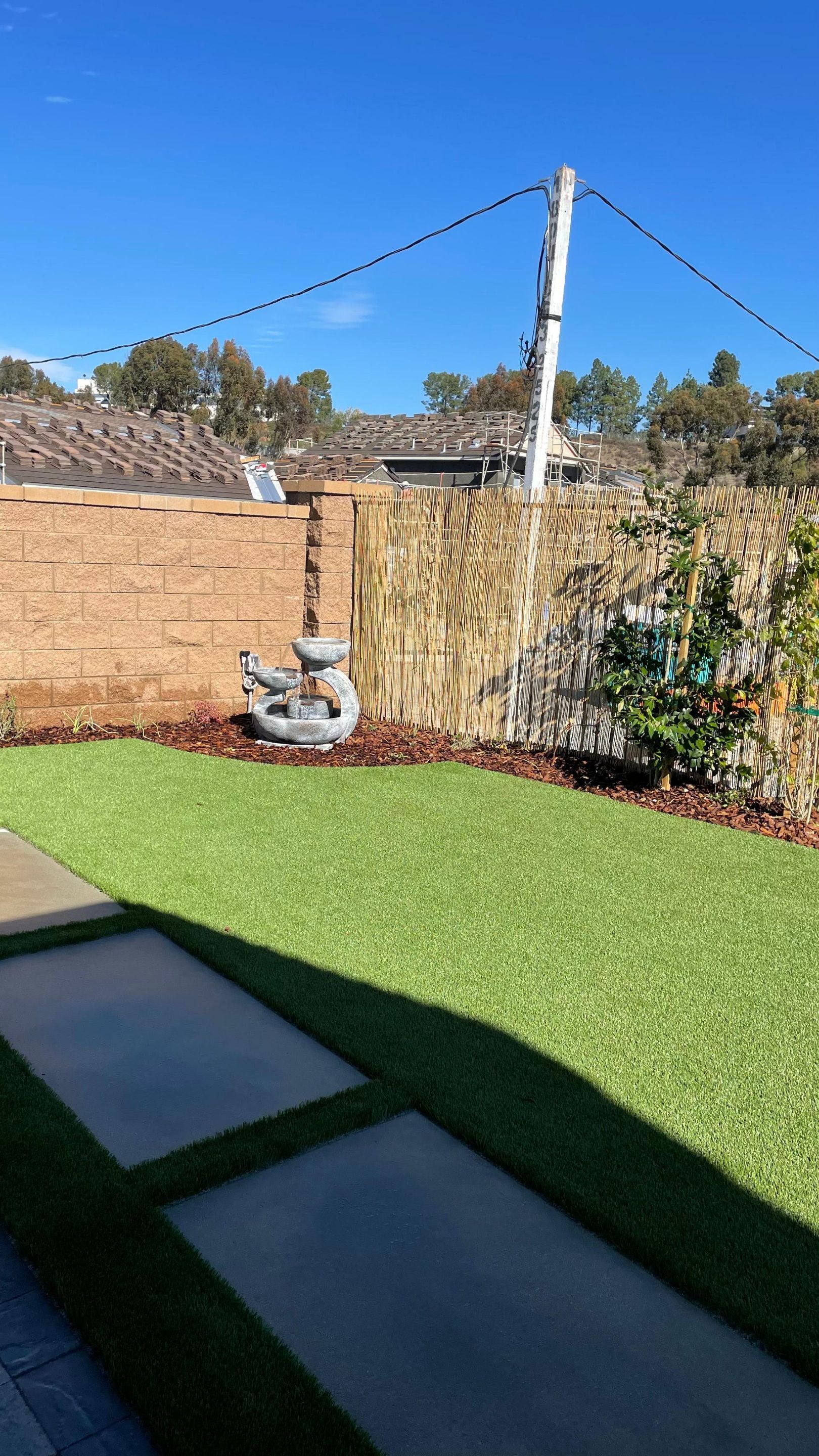 Backyard with green turf, stone walkway, brick wall, bamboo fence, and string lights.