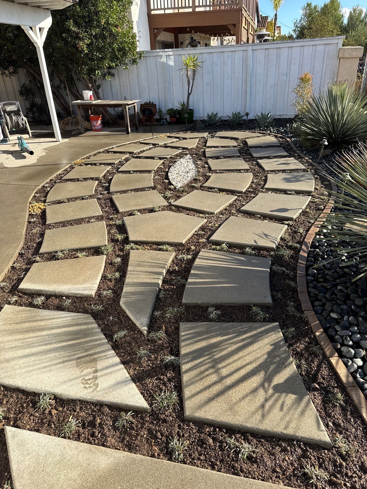 Stone walkway with curved design through a landscaped yard; surrounded by mulch and border rocks.