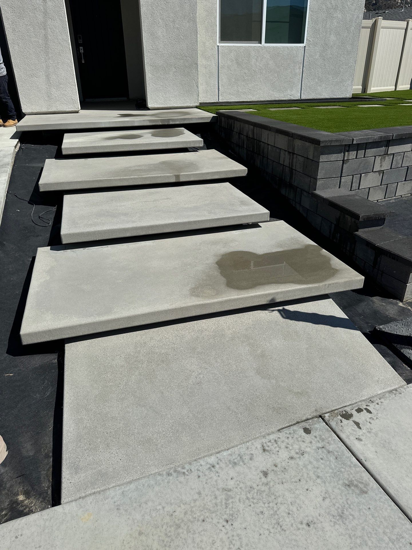Concrete steps leading up to a house entrance; dark door, retaining wall with grass.