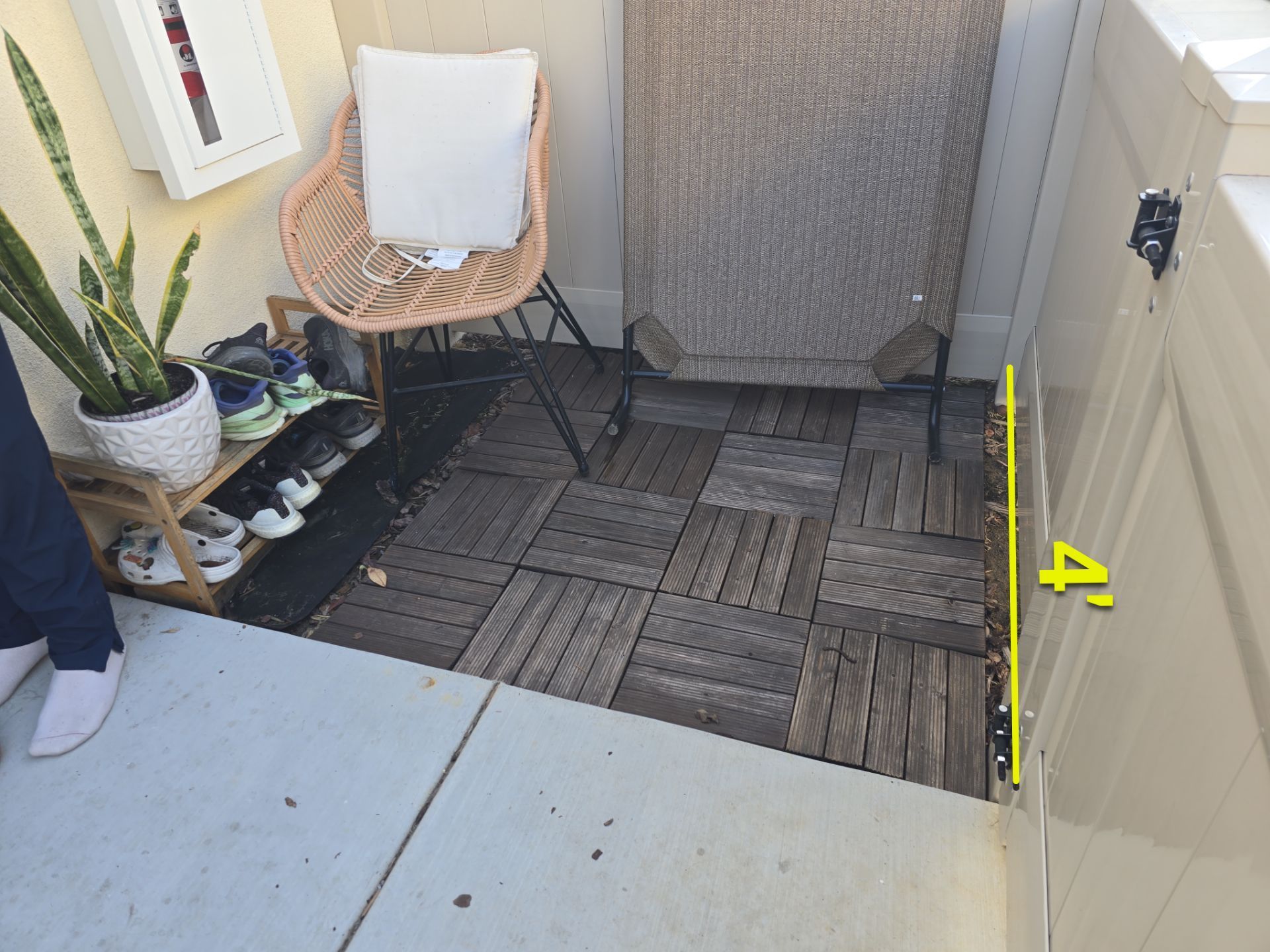 Outdoor patio with wooden floor tiles and chair, shoes, and potted plant.