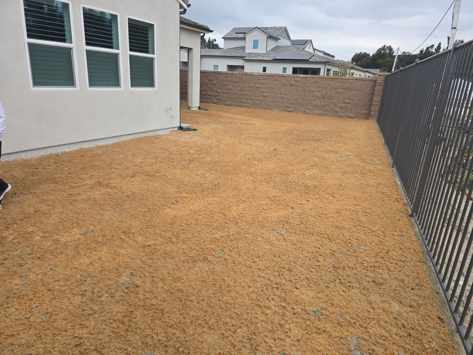 Empty backyard covered in light brown mulch, bordered by a fence and a house.