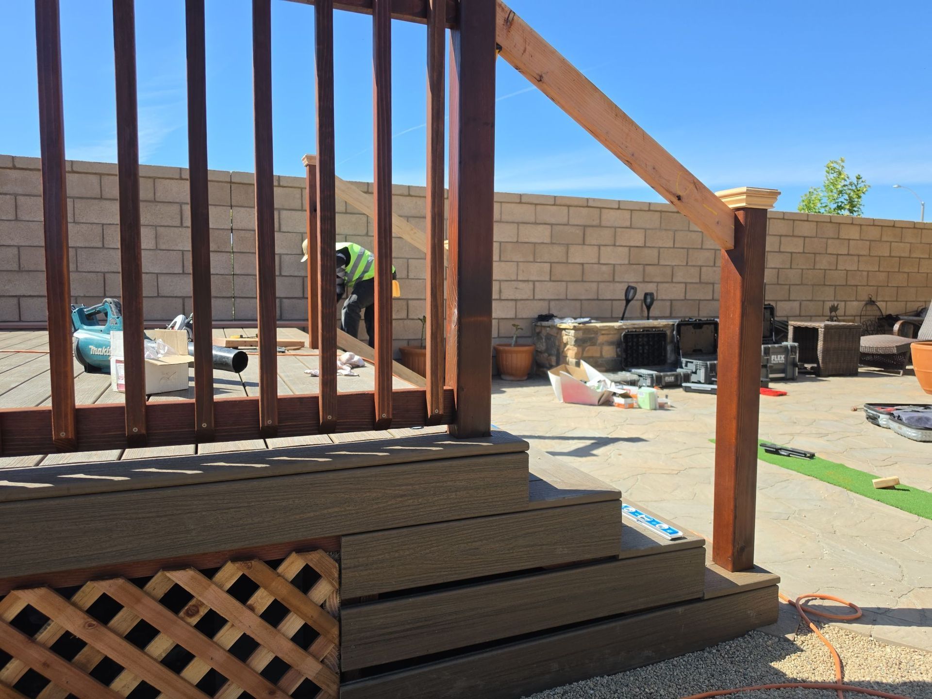 Wooden deck stairs and railing in a backyard, with a cinderblock wall and garden items in the background