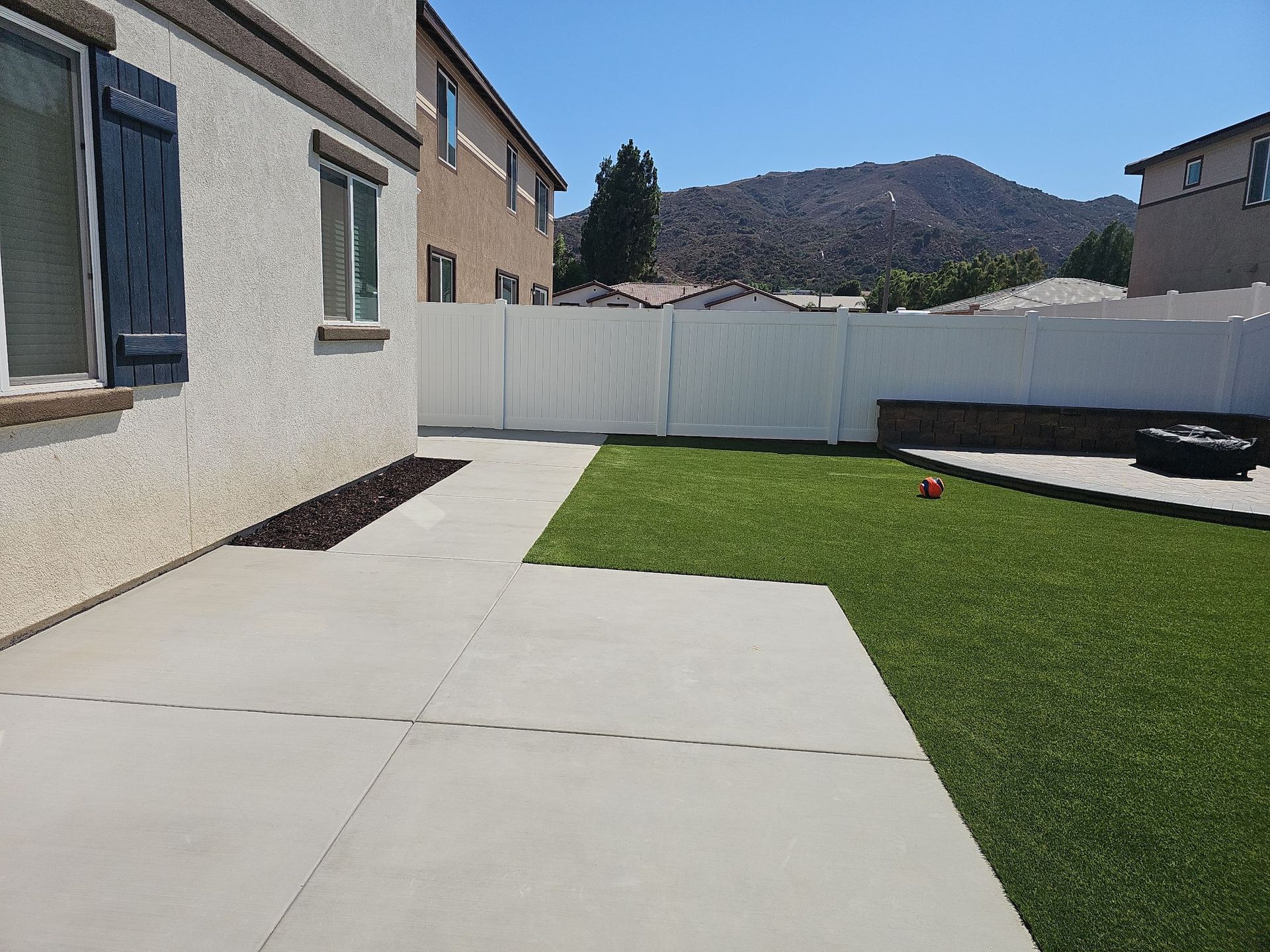 Backyard with concrete patio, artificial turf, white fence, and mountains in the background.