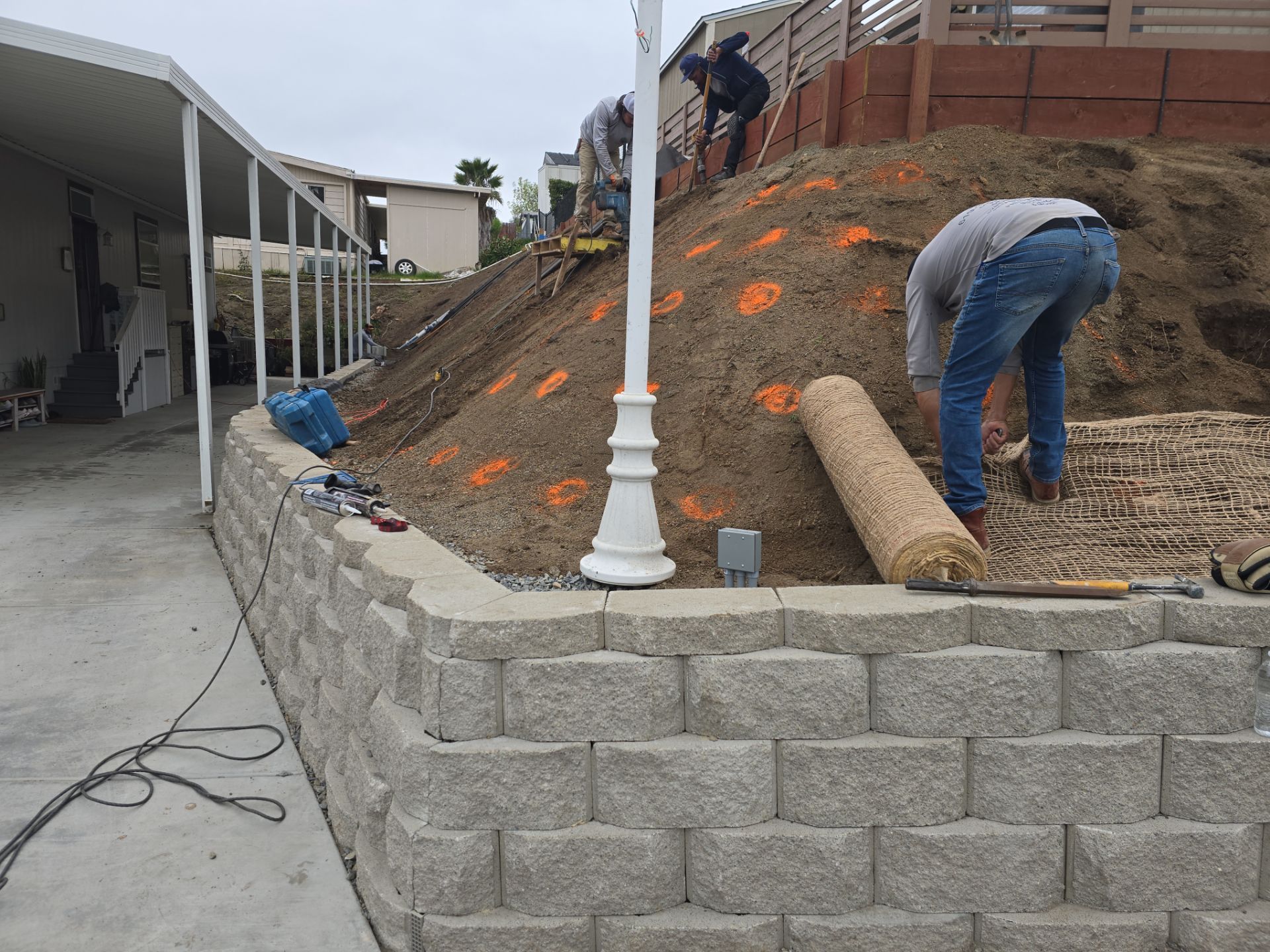 Workers building a retaining wall on a hillside covered with mulch.