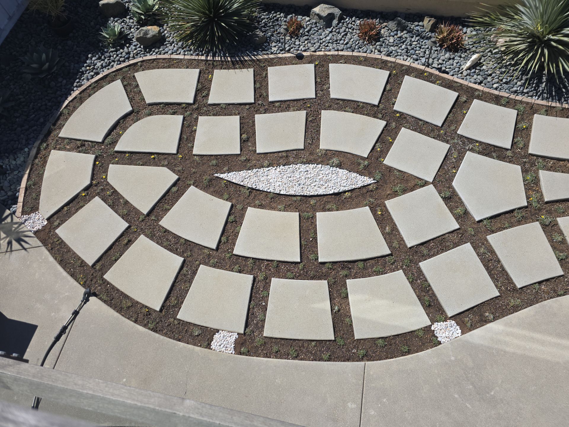 Stone walkway with square pavers and gravel-filled center bed, surrounded by mulch and greenery.
