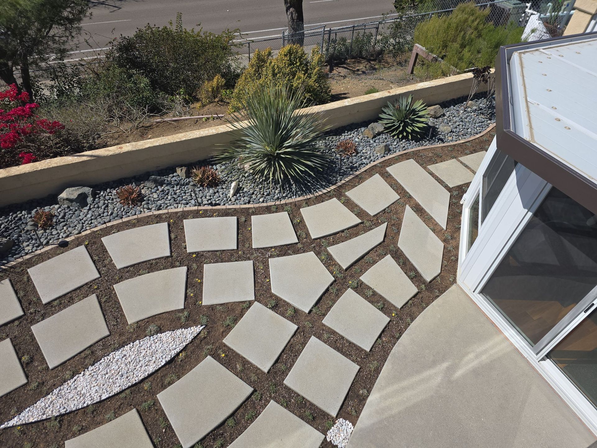 Overhead view of a patio with a stone pathway leading to a window near a landscaped garden.