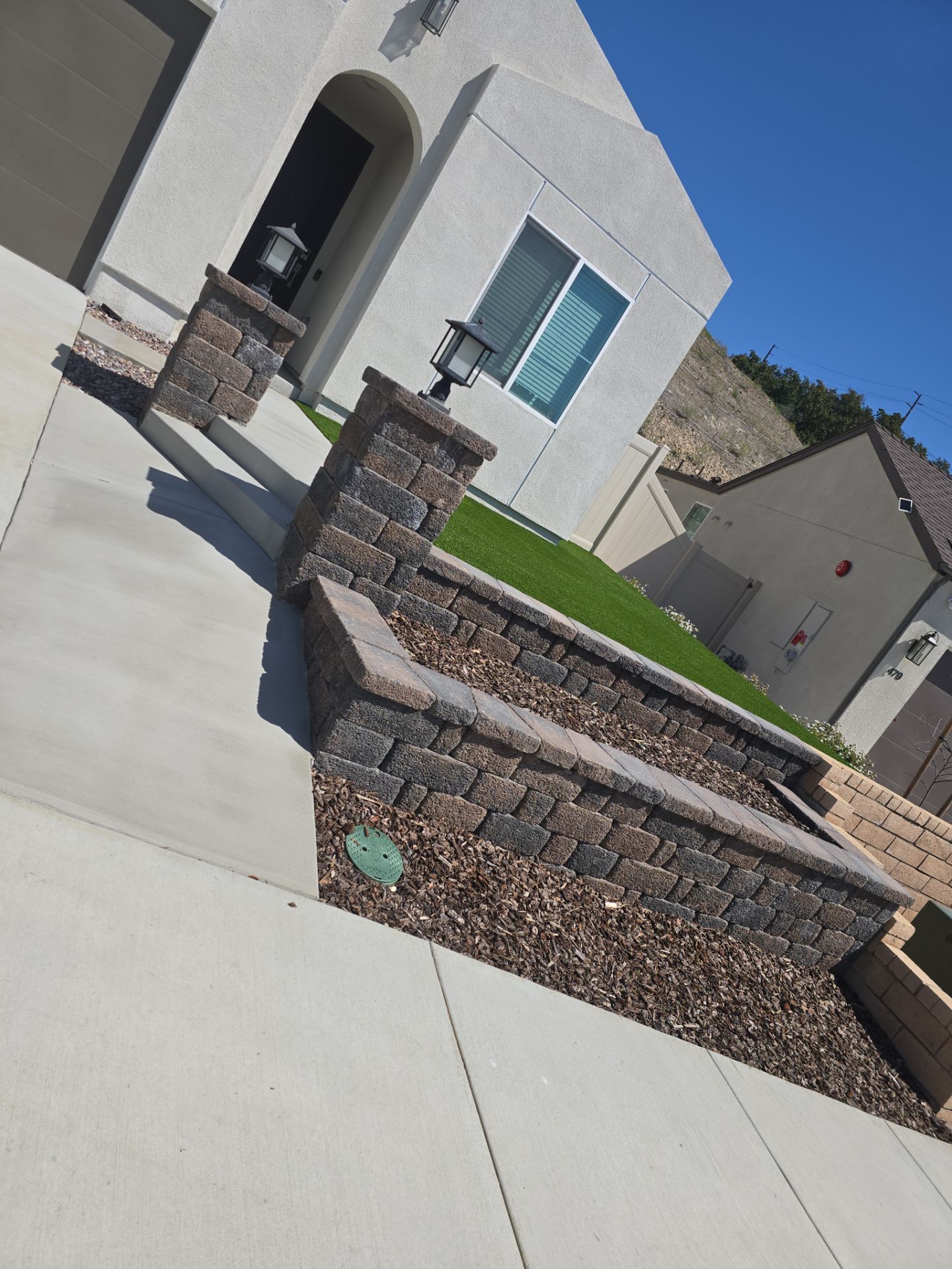 A tan home with a brick wall and a small patch of grass. A driveway leads up to the house.