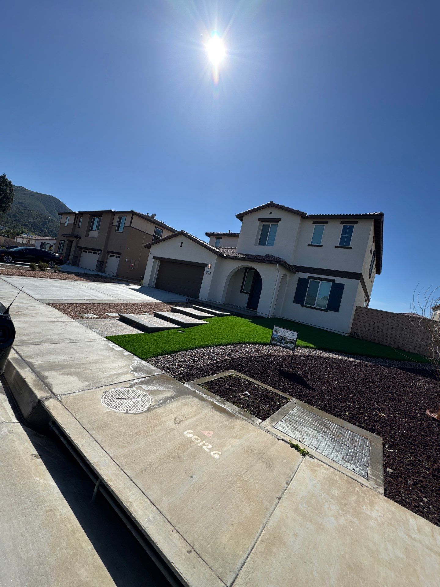 Two-story beige house with a garage and green lawn under a bright blue sky.