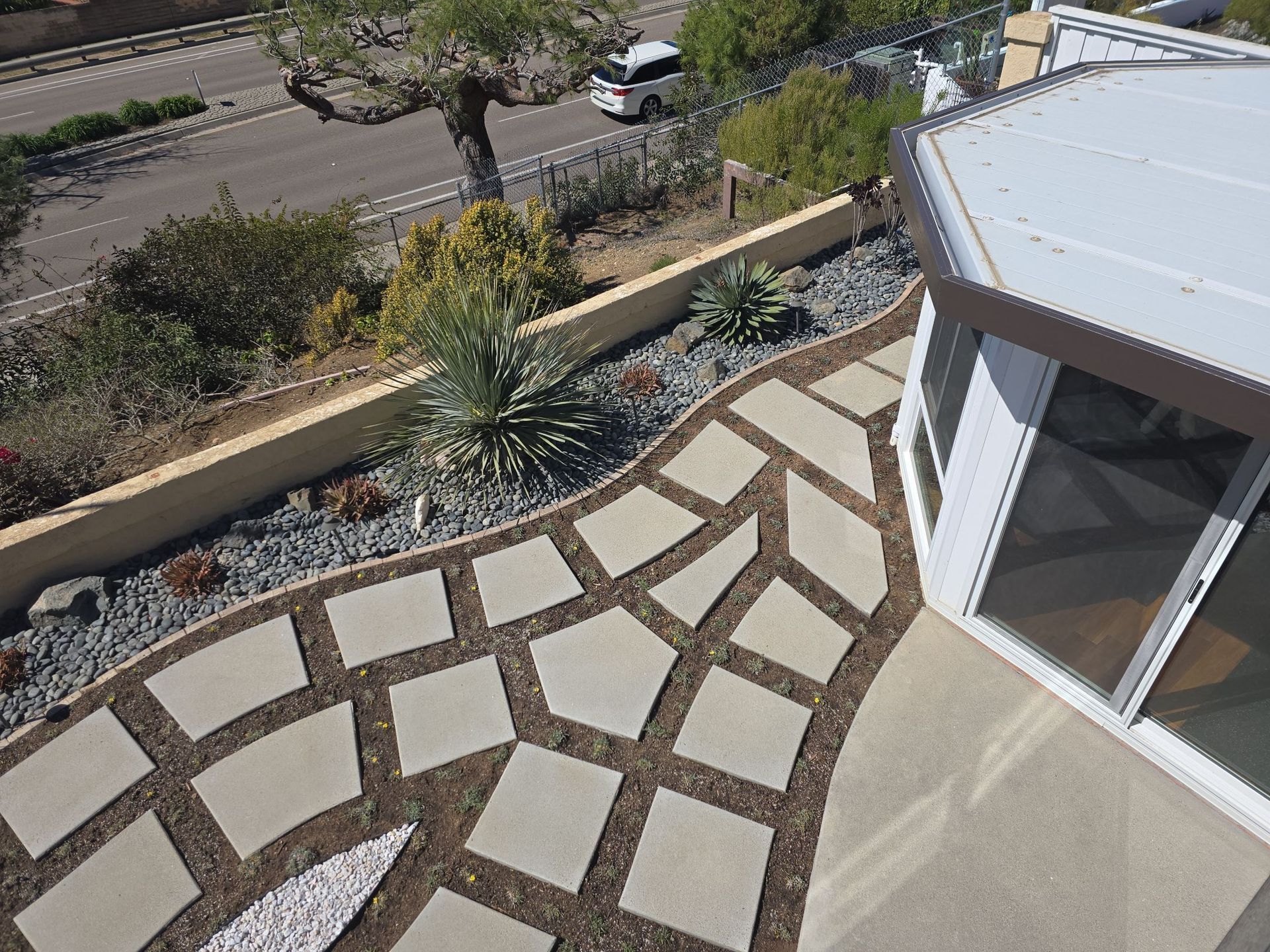 Overhead view of patio with square stepping stones, landscaping, and adjacent road.