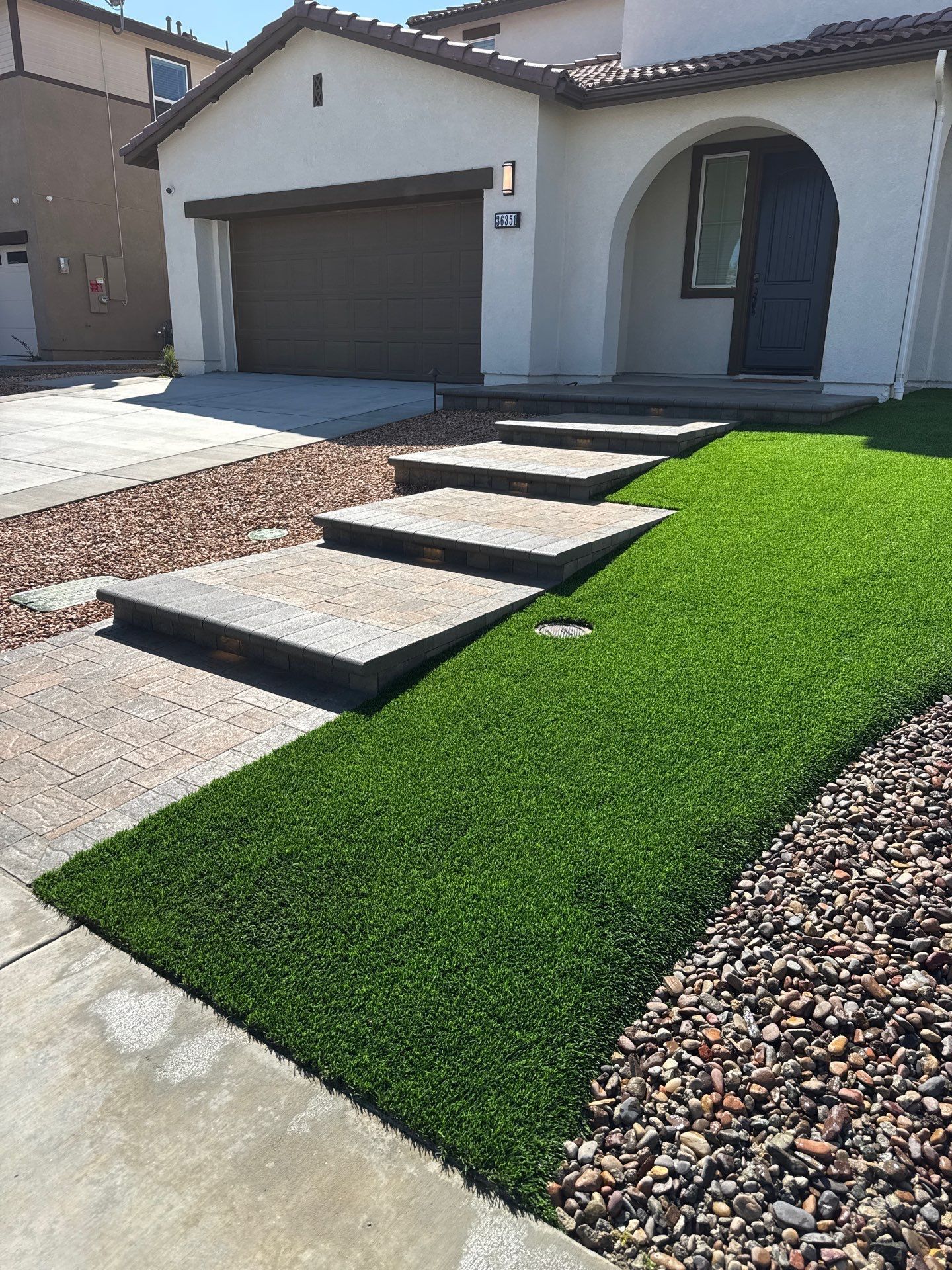 Exterior view of a house with stone steps, a brown garage door, green turf, and landscaping.
