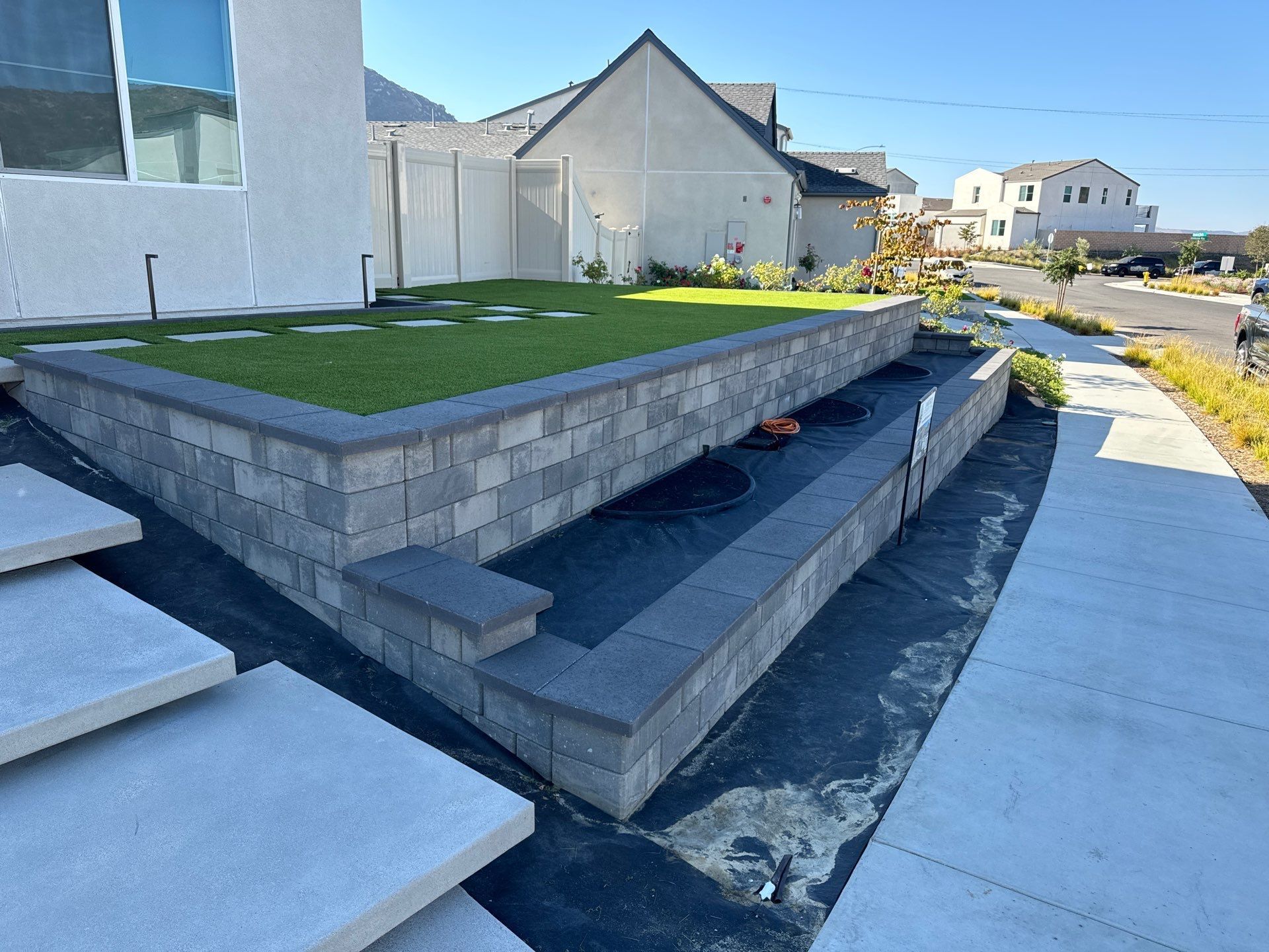 Gray brick retaining walls with artificial turf and concrete steps along a residential sidewalk.
