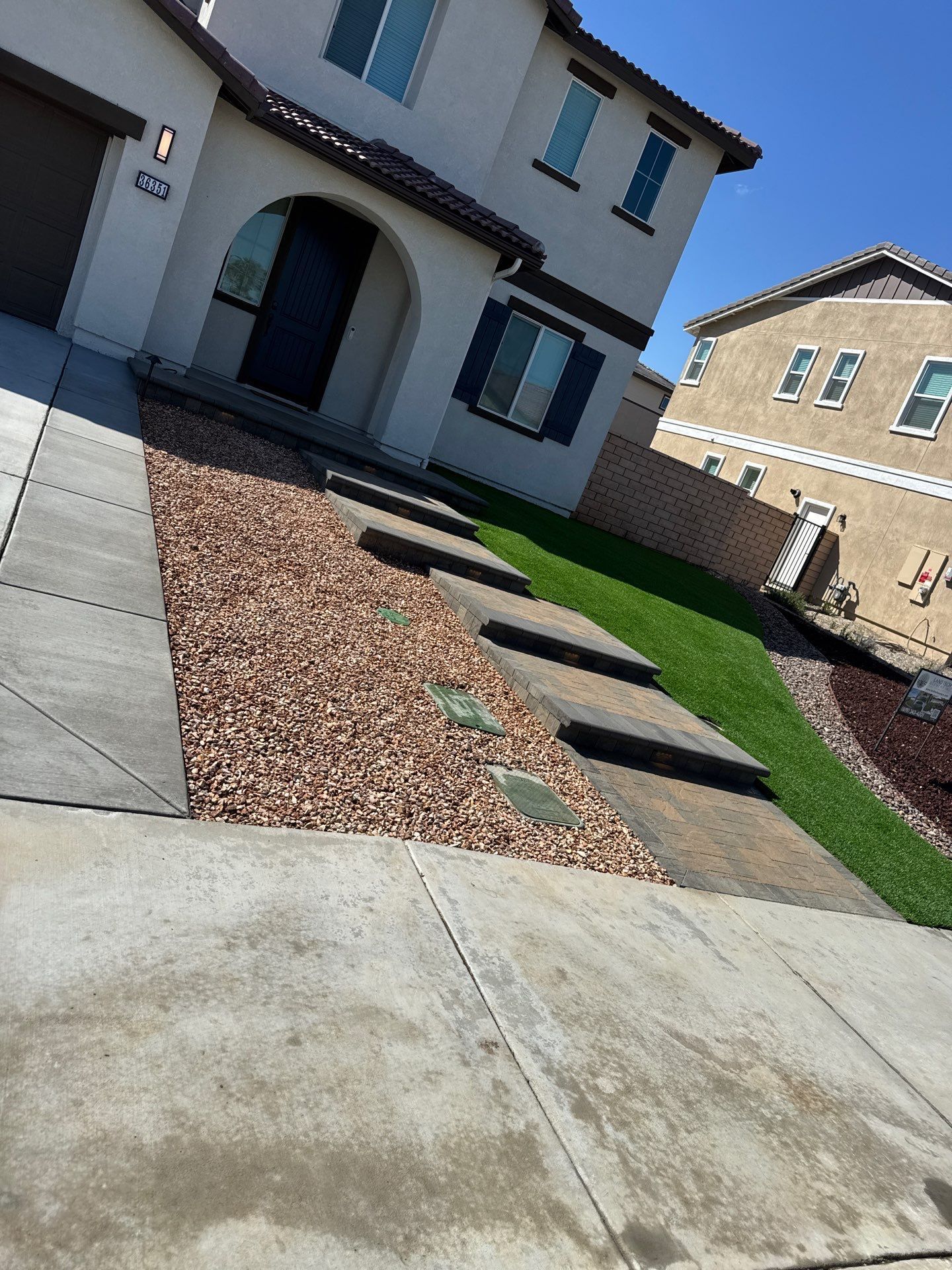Beige house with a gravel bed, stepping stones, and a strip of green grass.