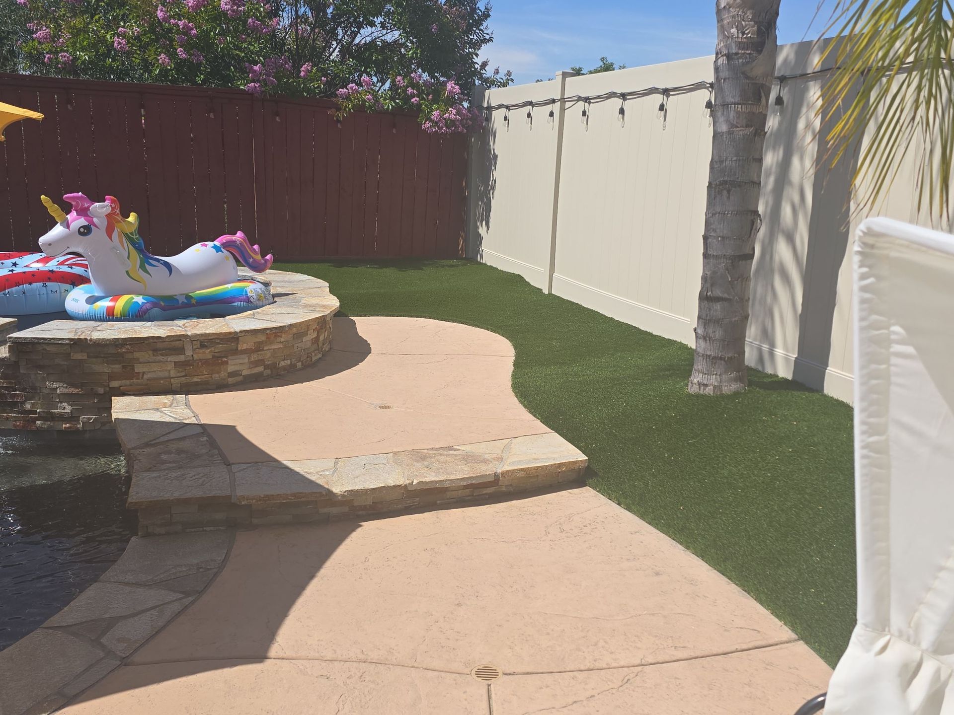 Backyard with pool, steps, and artificial turf. Unicorn float in the pool. Fences surround the area.
