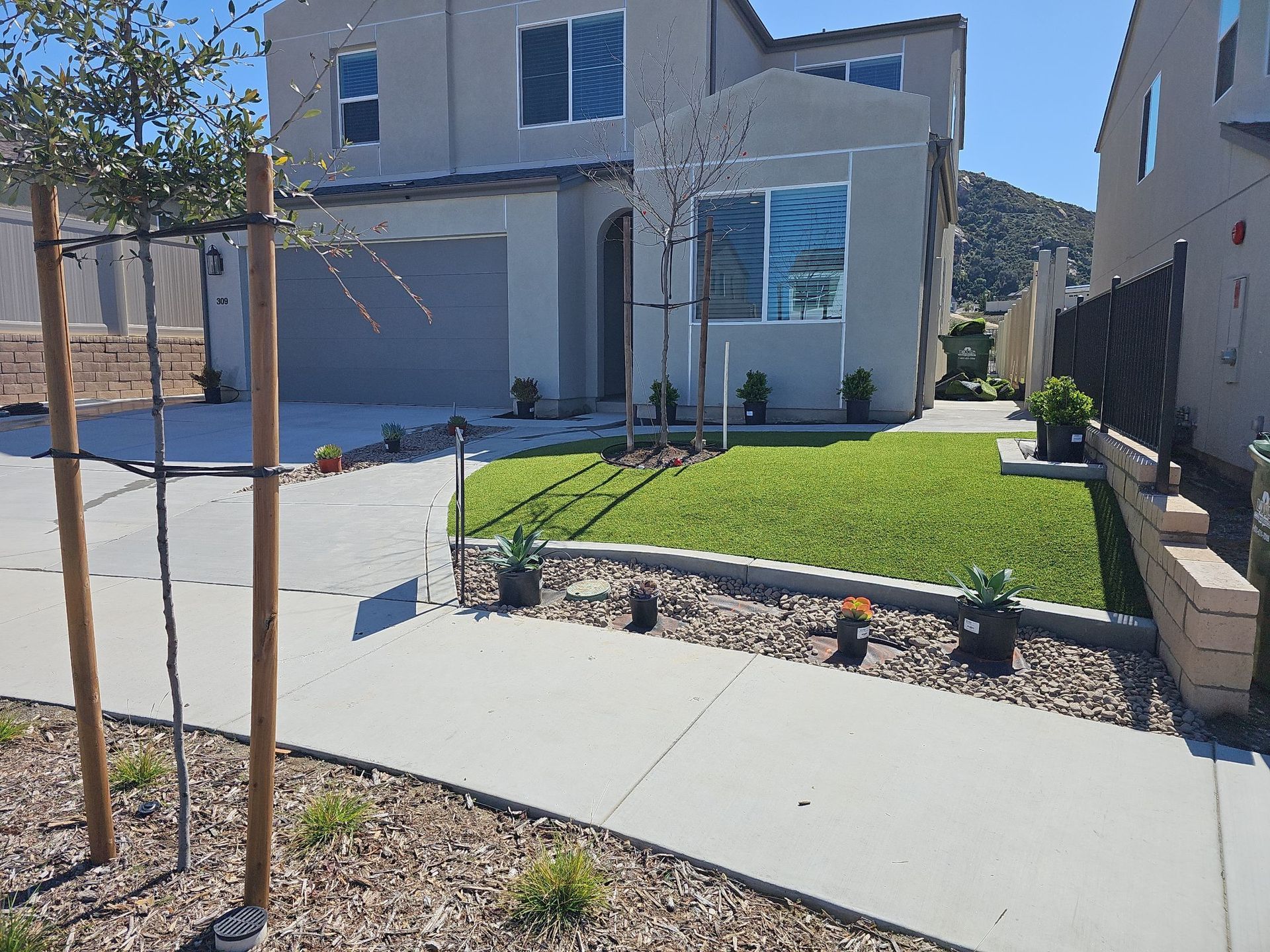 Two-story house with green lawn, sidewalk, driveway, and landscaping in front. Mountains visible in the background.