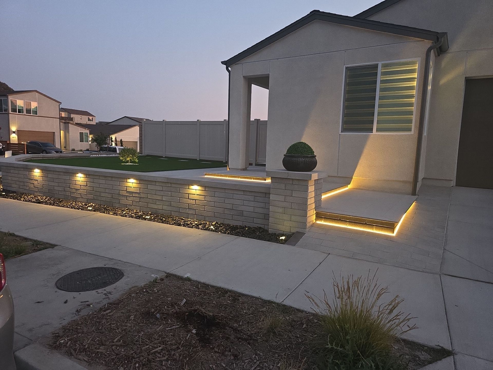 Exterior of a house at dusk with illuminated stone wall and steps.