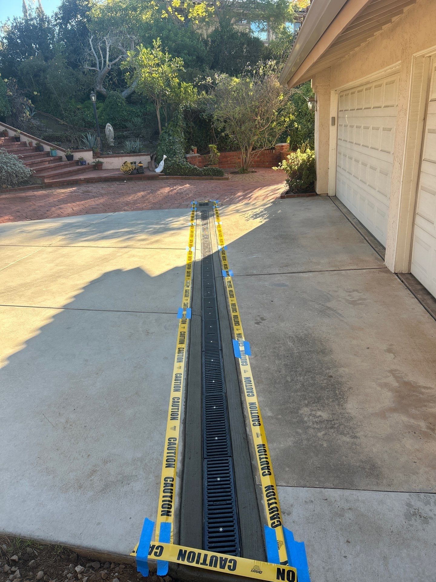 Measuring tape stretched along a concrete driveway beside a garage in a sunny yard
