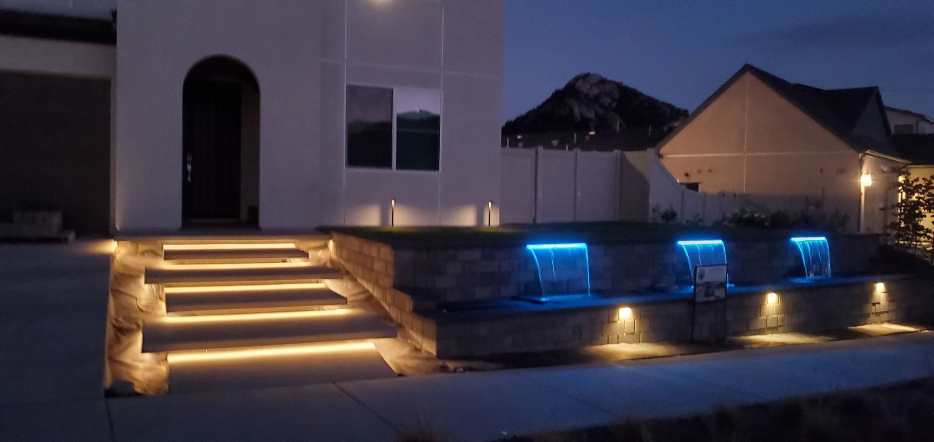 Illuminated house exterior at night with steps and waterfall features.