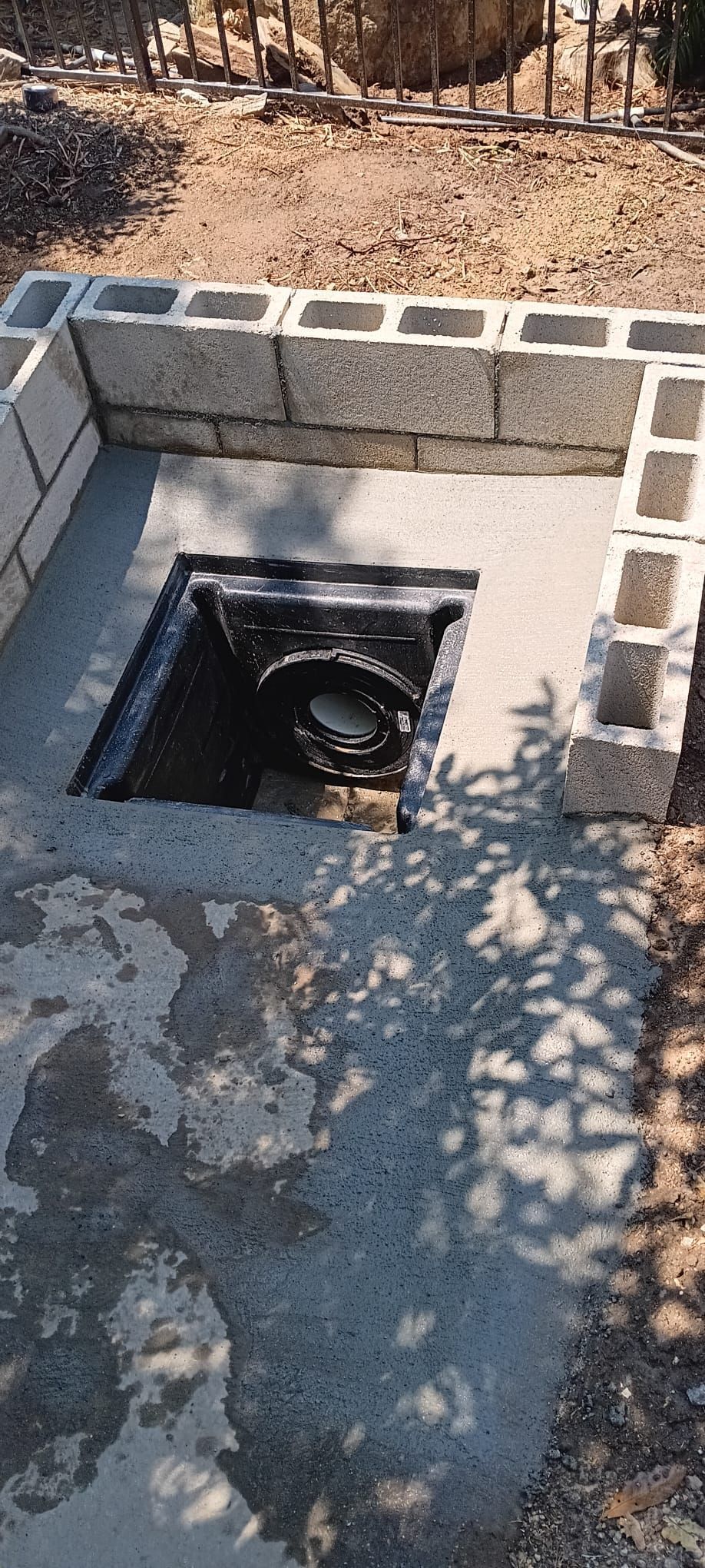 Concrete-lined square pit with exposed pipe opening in an outdoor dirt area