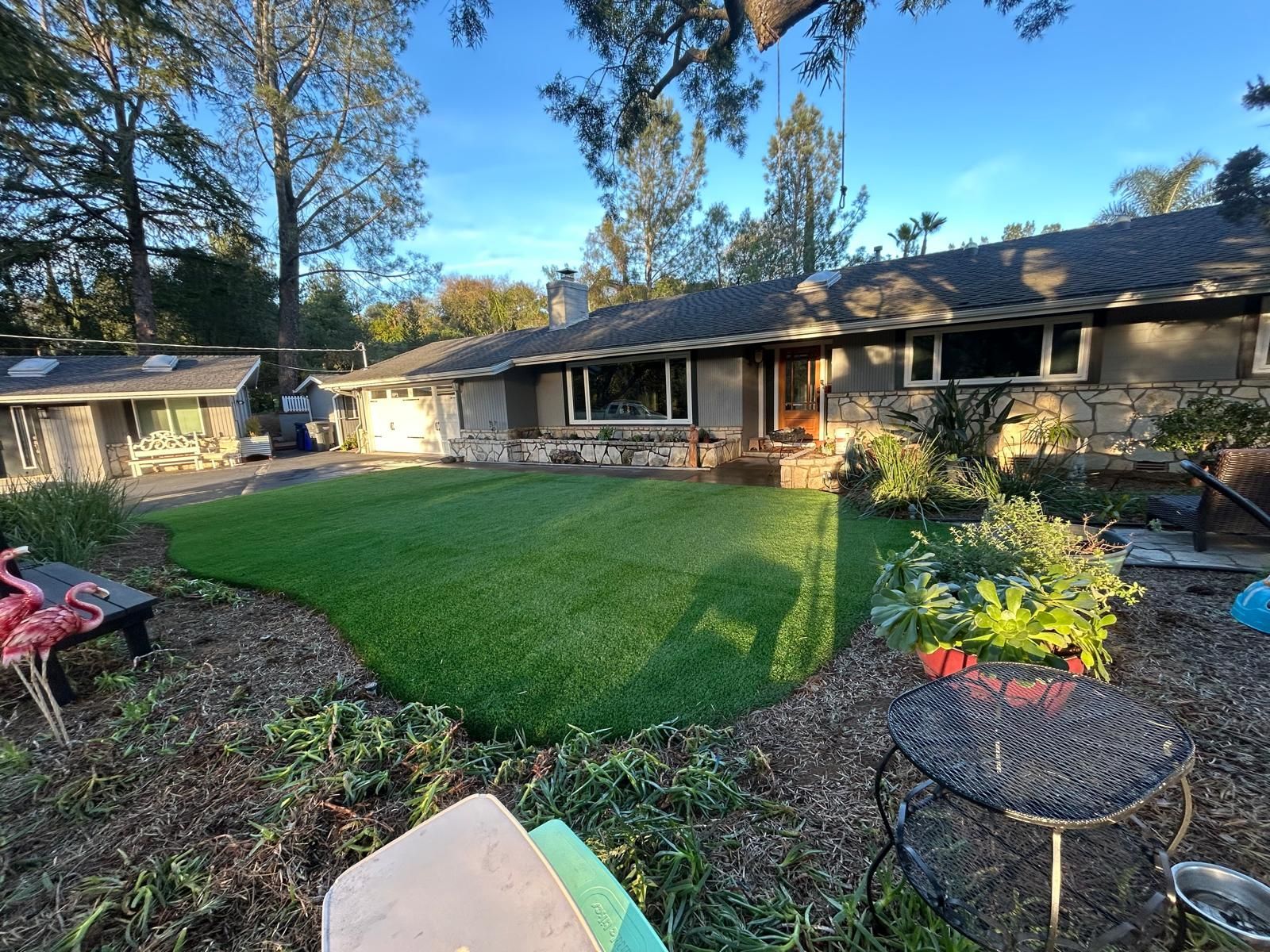House with green lawn, stone facade, and trees under a blue sky.