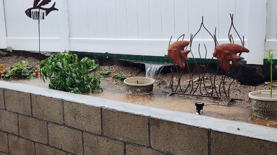 Backyard water feature overflowing during rain, with fish weathervane and decorative elements.
