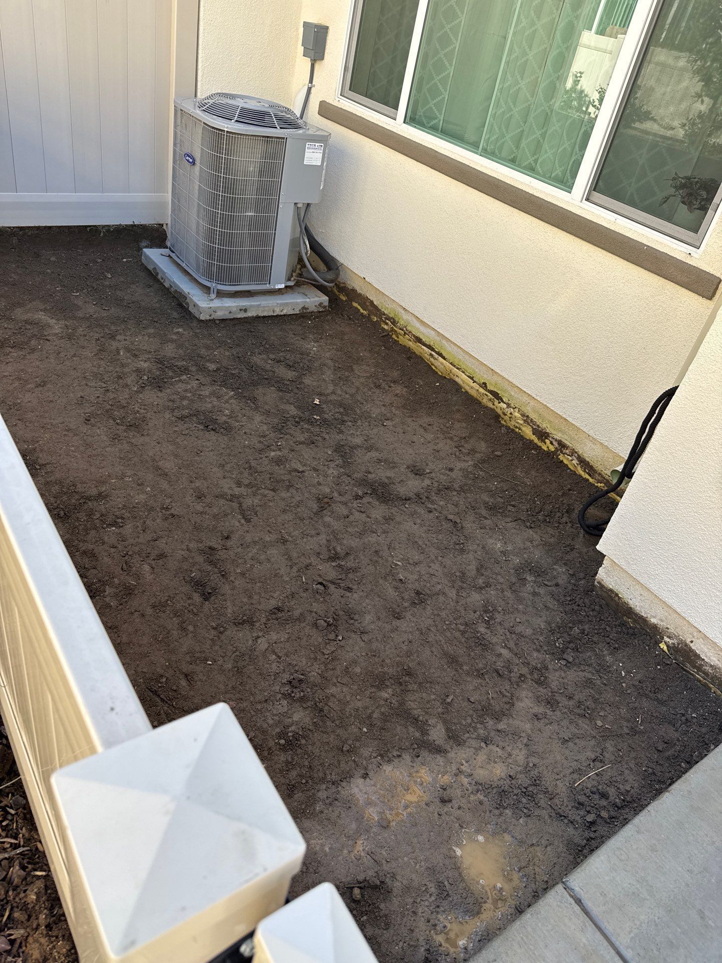 Small backyard with a dirt patch, air conditioner, and white fence.