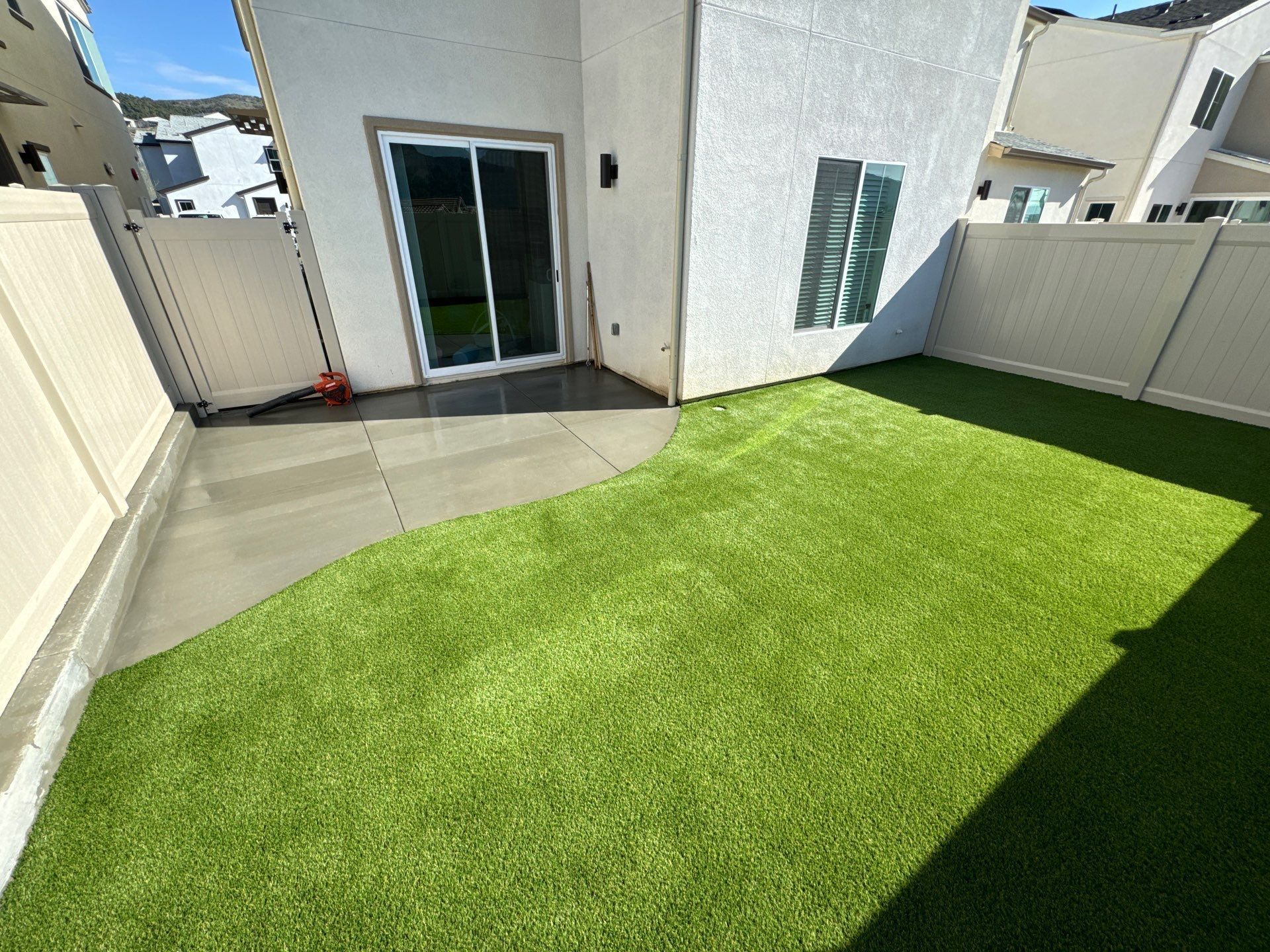 Backyard with concrete patio, artificial green grass, and white fence.