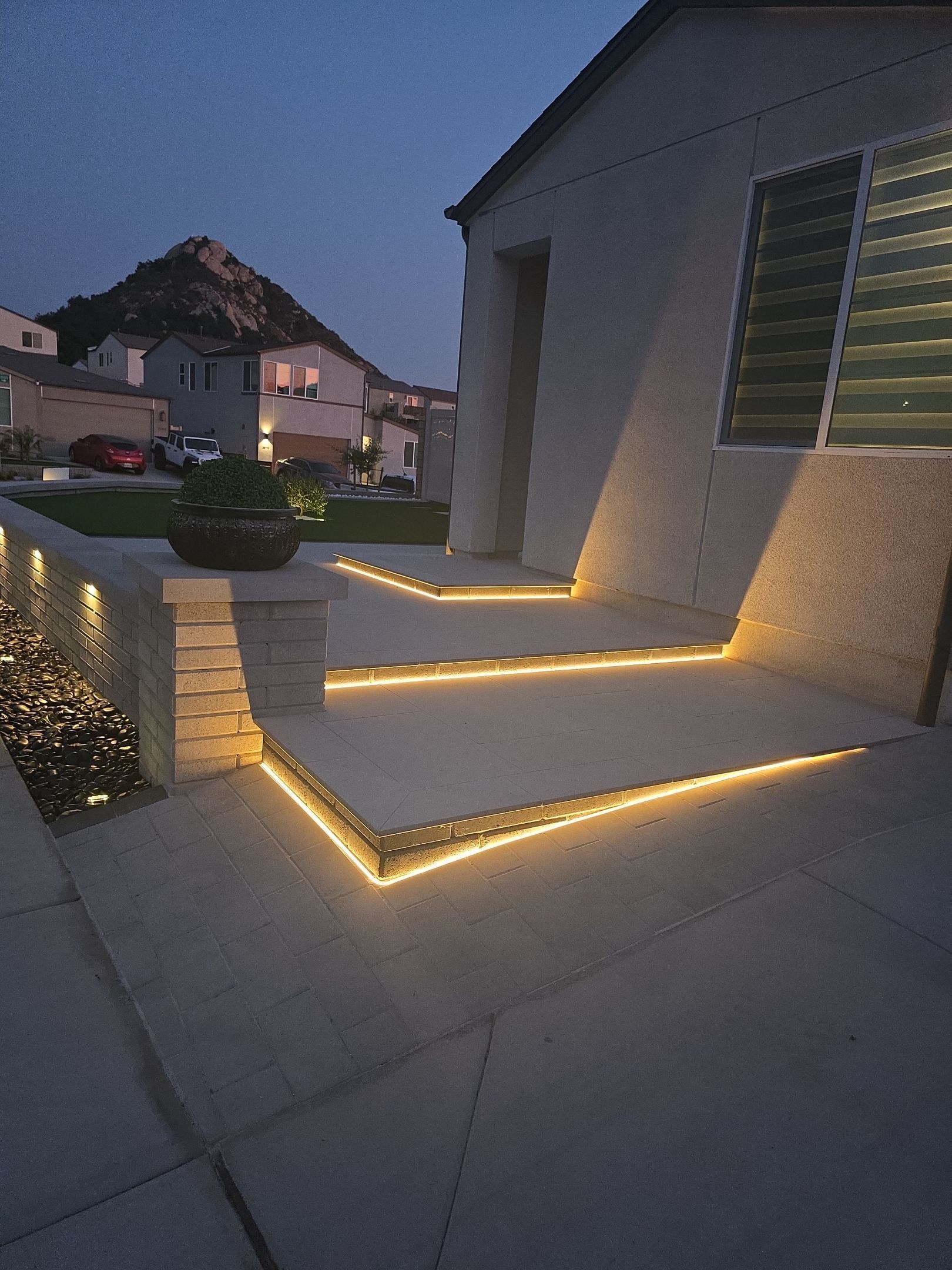 Exterior of a house at dusk, lit steps with warm lights, neighborhood in the background.