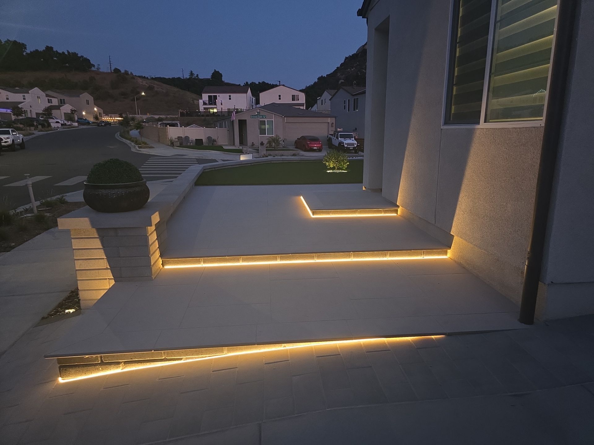 Exterior of a house at dusk. Lit steps and ledges in front with a neighborhood street in the background.