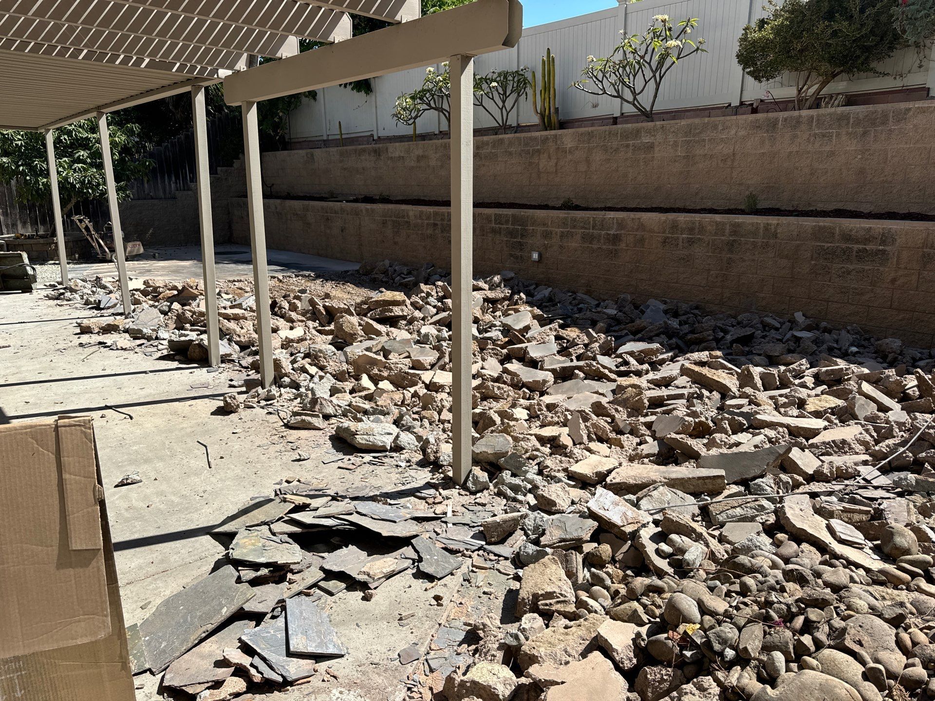 Debris pile on a patio under a shaded structure, next to a retaining wall and plants.