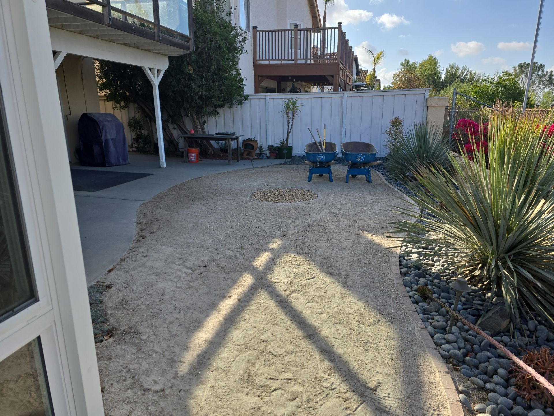 Backyard with gravel ground, blue chairs, and a white fence.