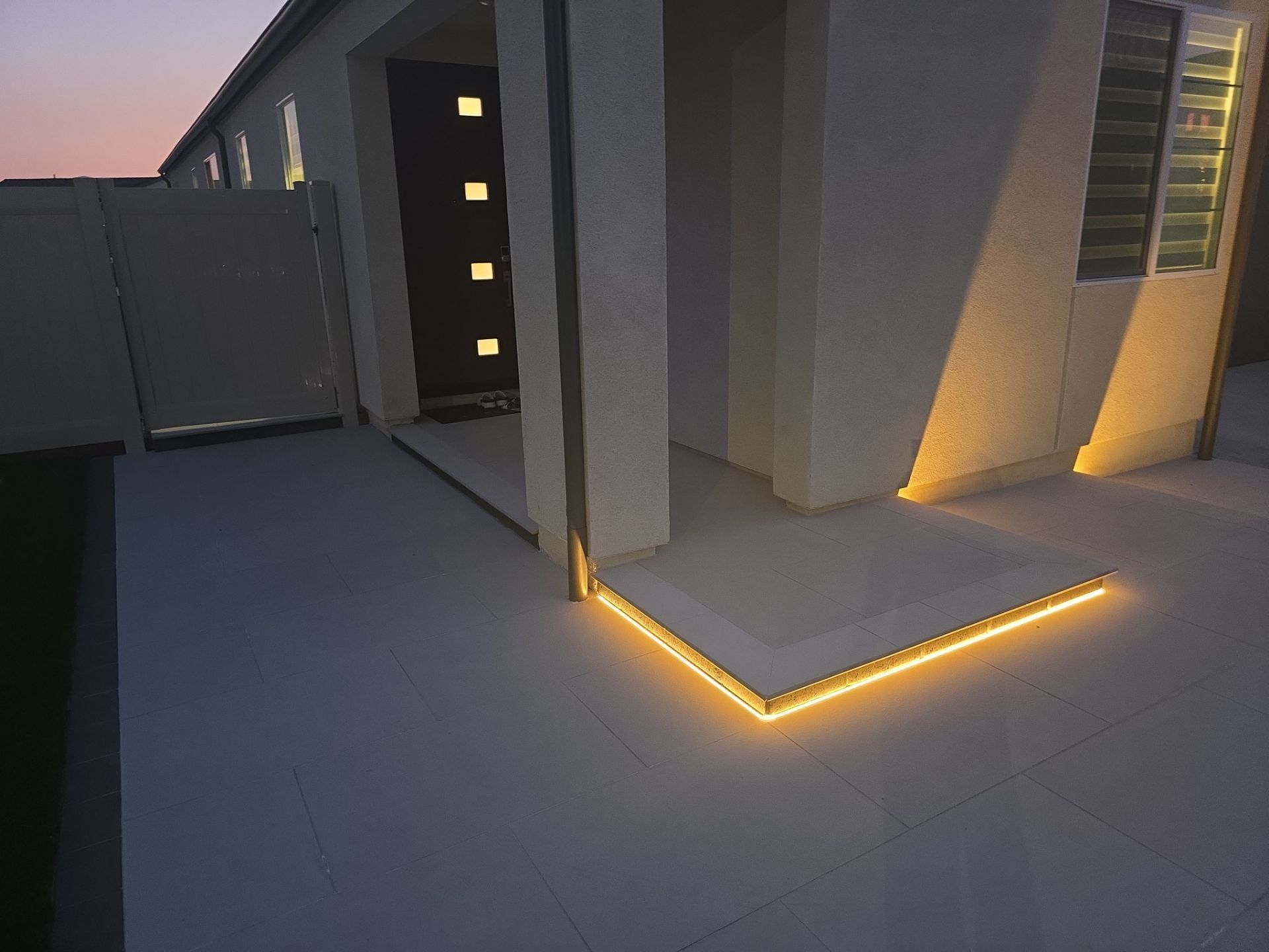 Exterior of a home at dusk with warm yellow lighting outlining the entryway and porch.