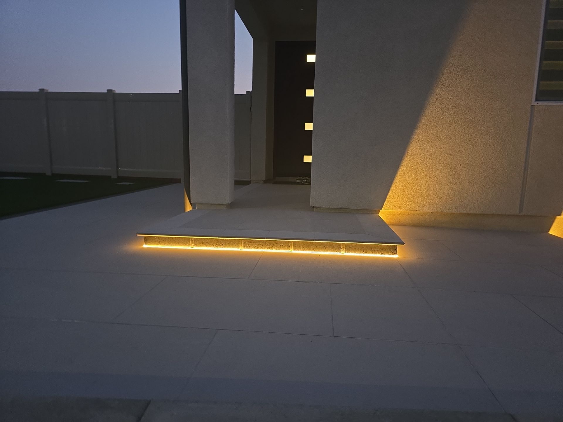 Illuminated entrance of a modern home with step lighting glowing against the concrete at dusk.