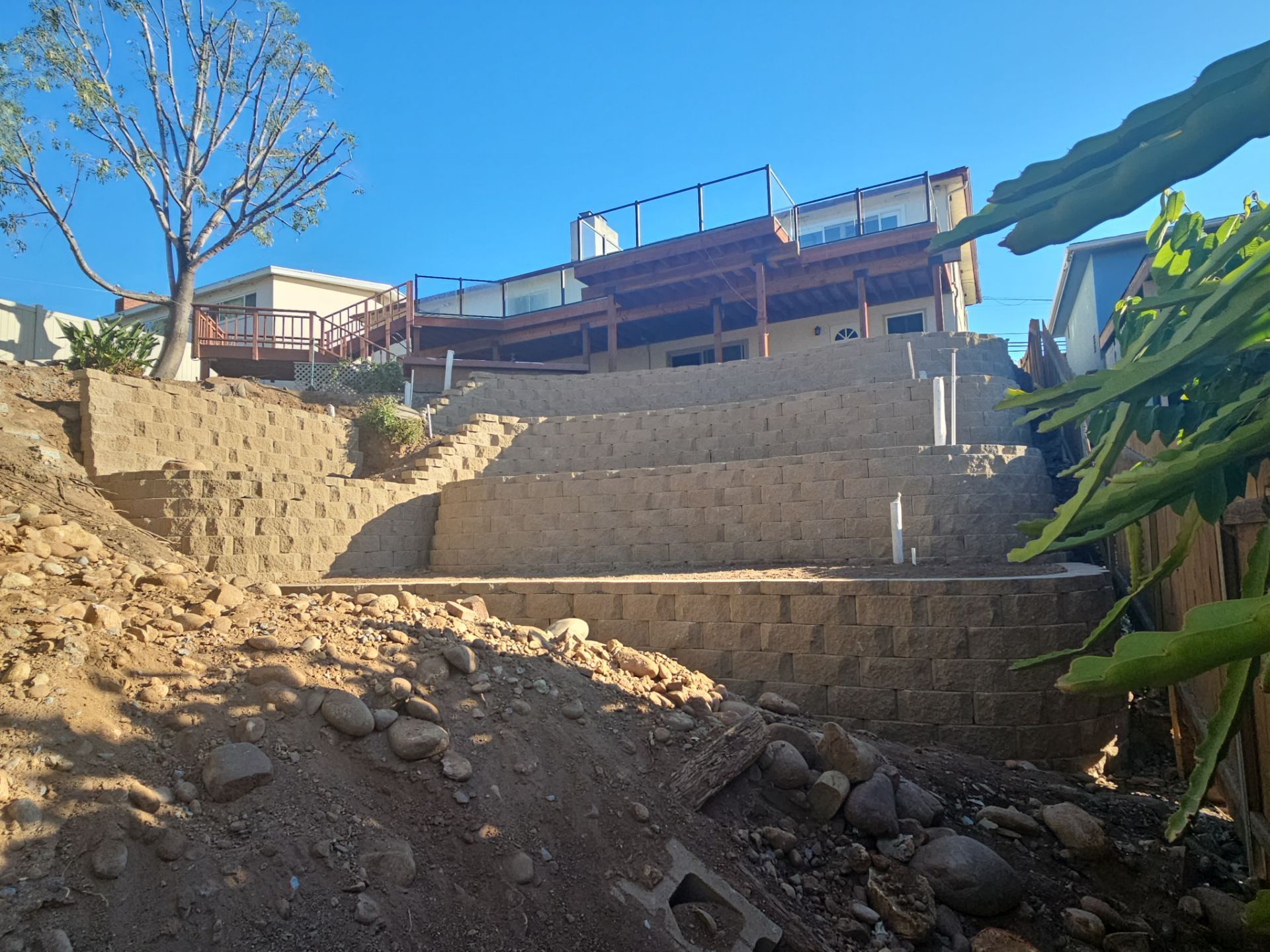 A tiered retaining wall with steps leading up to a house with a deck. Construction debris is visible.
