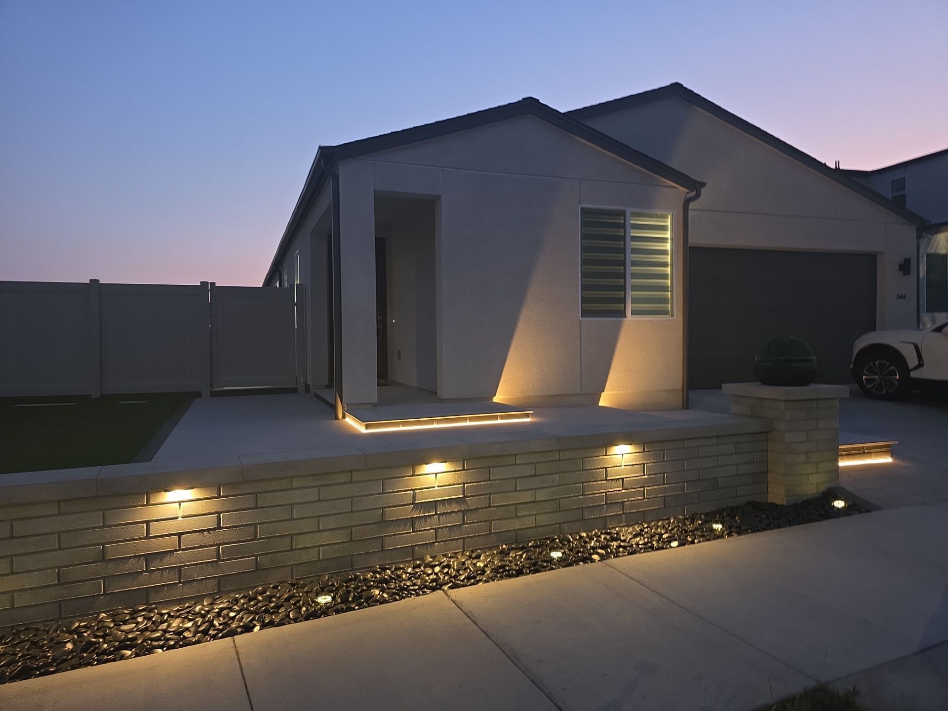 House exterior at dusk, illuminated wall with spotlights, driveway.