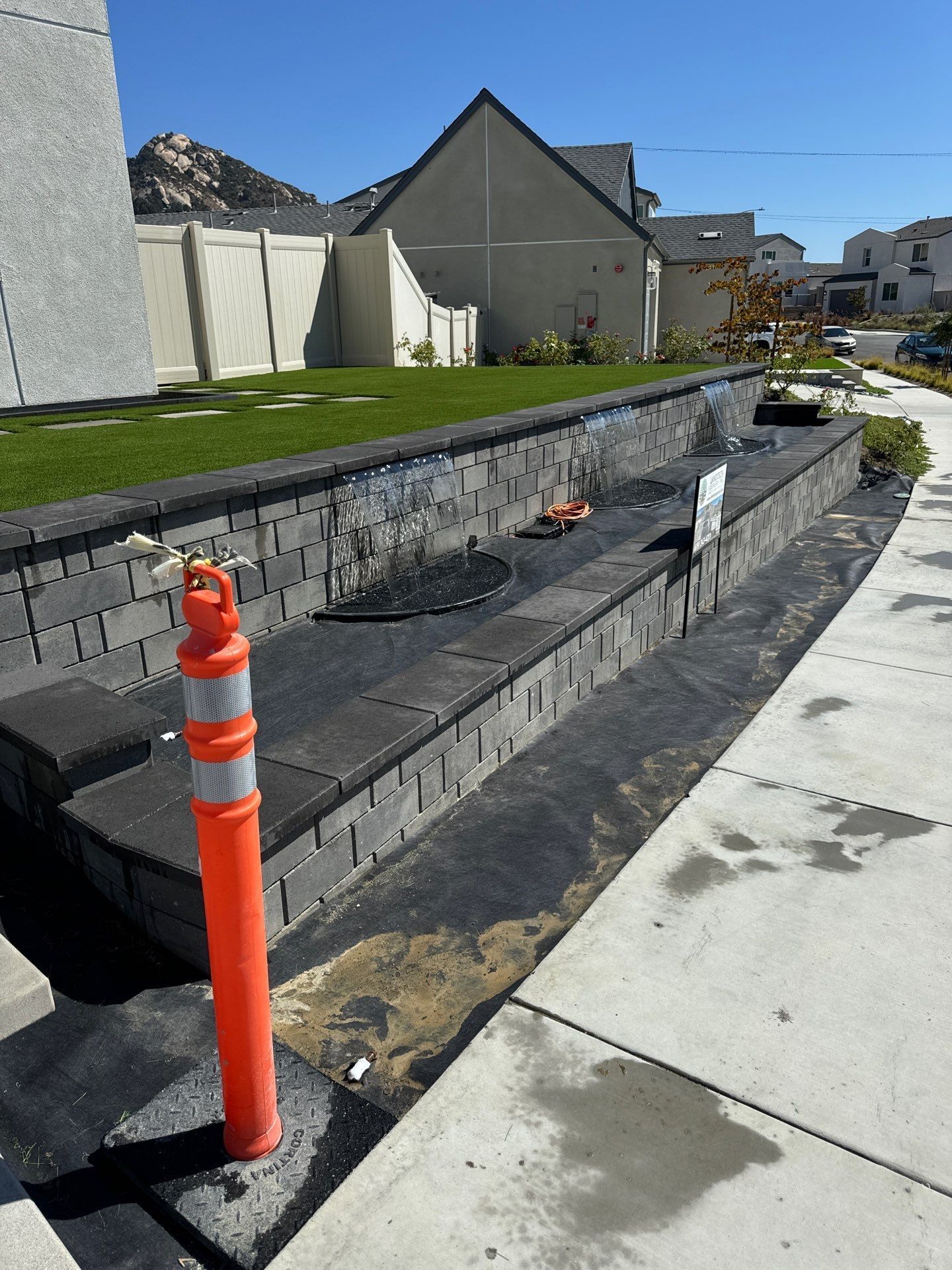 Brick retaining wall under construction with orange safety cone on a sunny day.
