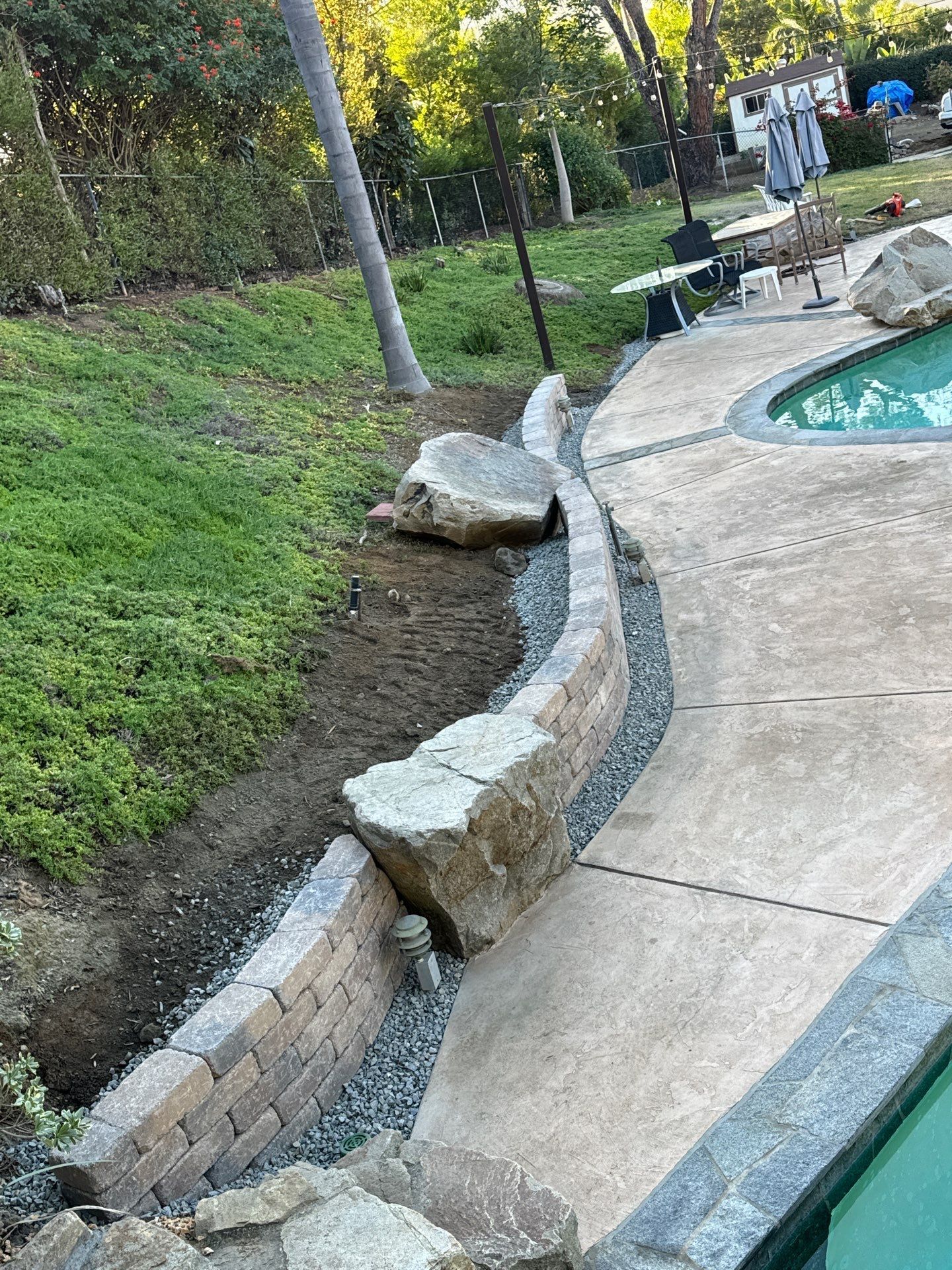 Stone retaining wall and pathway beside a swimming pool in a yard.