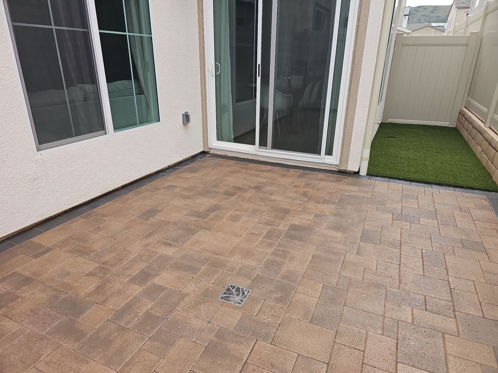 Patio with brick pavers, sliding glass door, and patch of artificial turf.