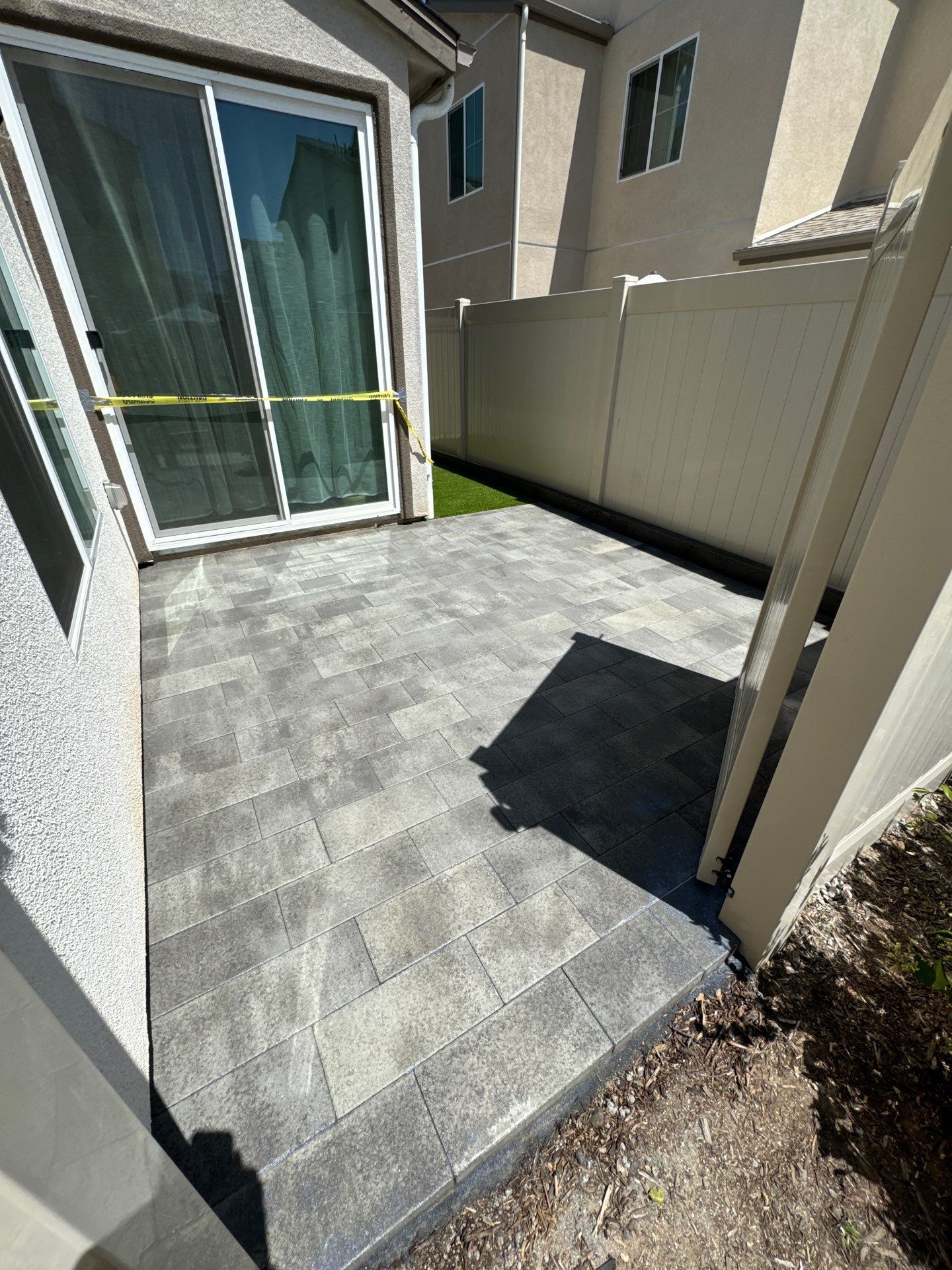 Grey paver patio outside a sliding glass door and adjacent to a white fence.